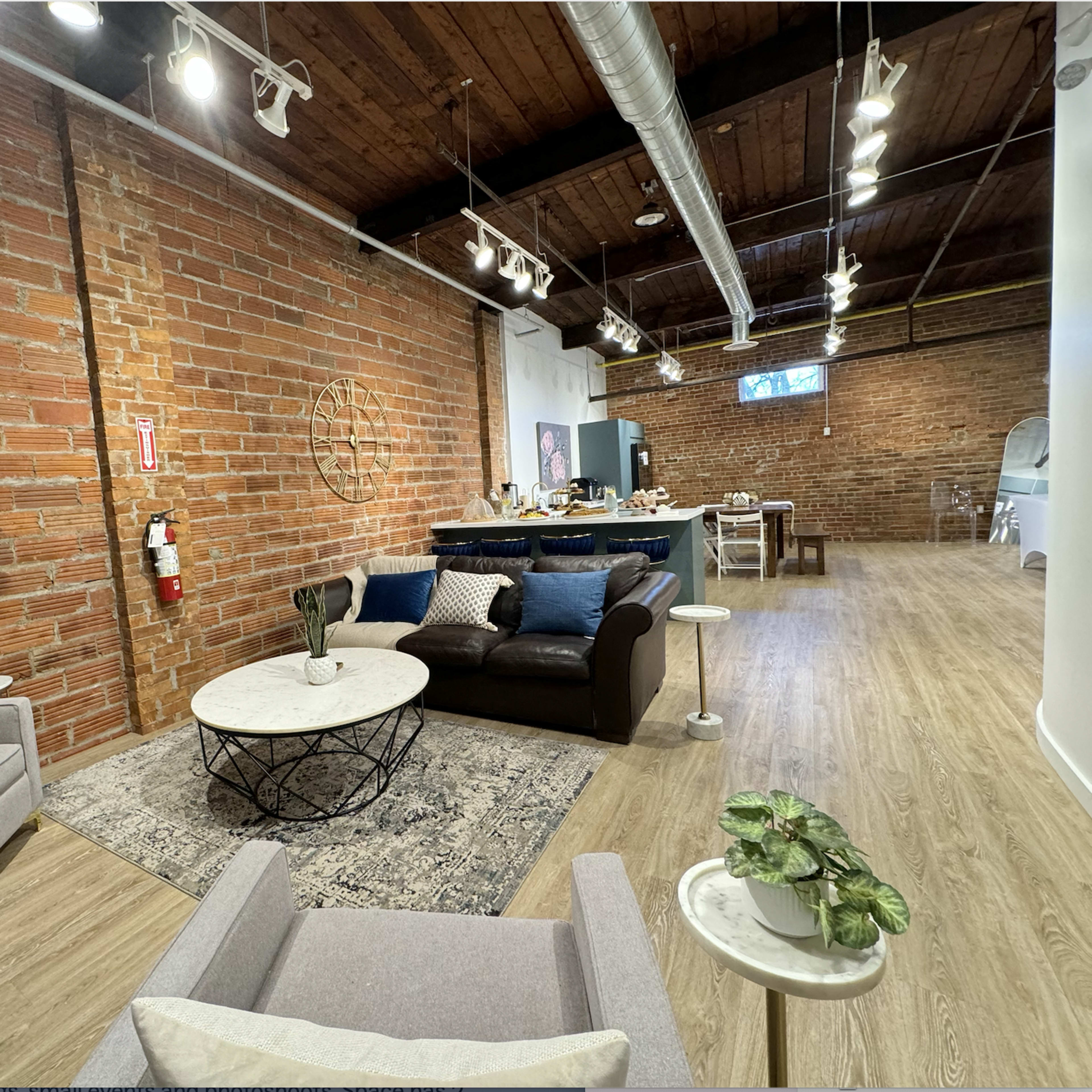 A spacious living area with exposed brick walls, a modern sofa, a coffee table, and a dining area in the background.