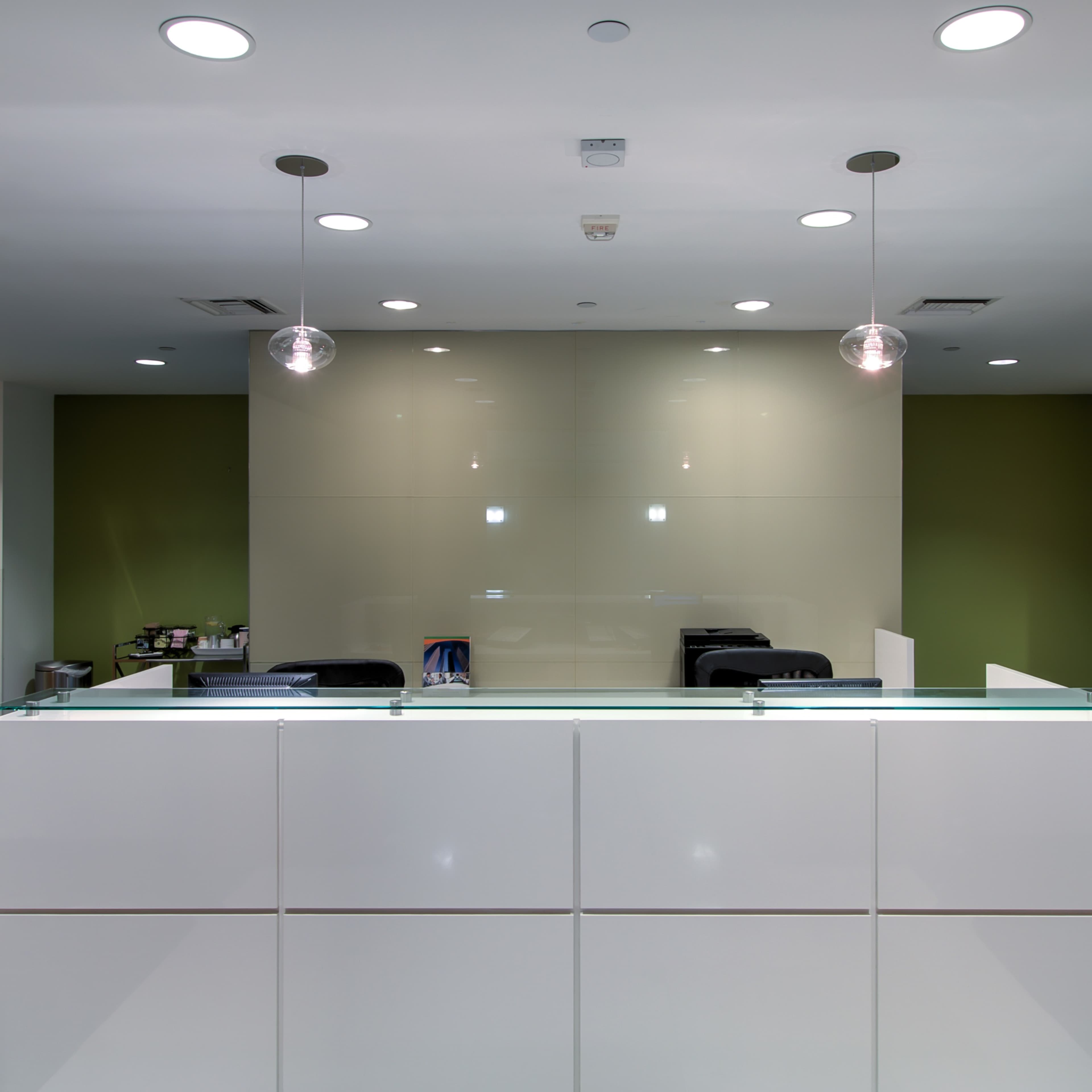 A modern reception area with a white front desk, green accent walls, and overhead lighting.