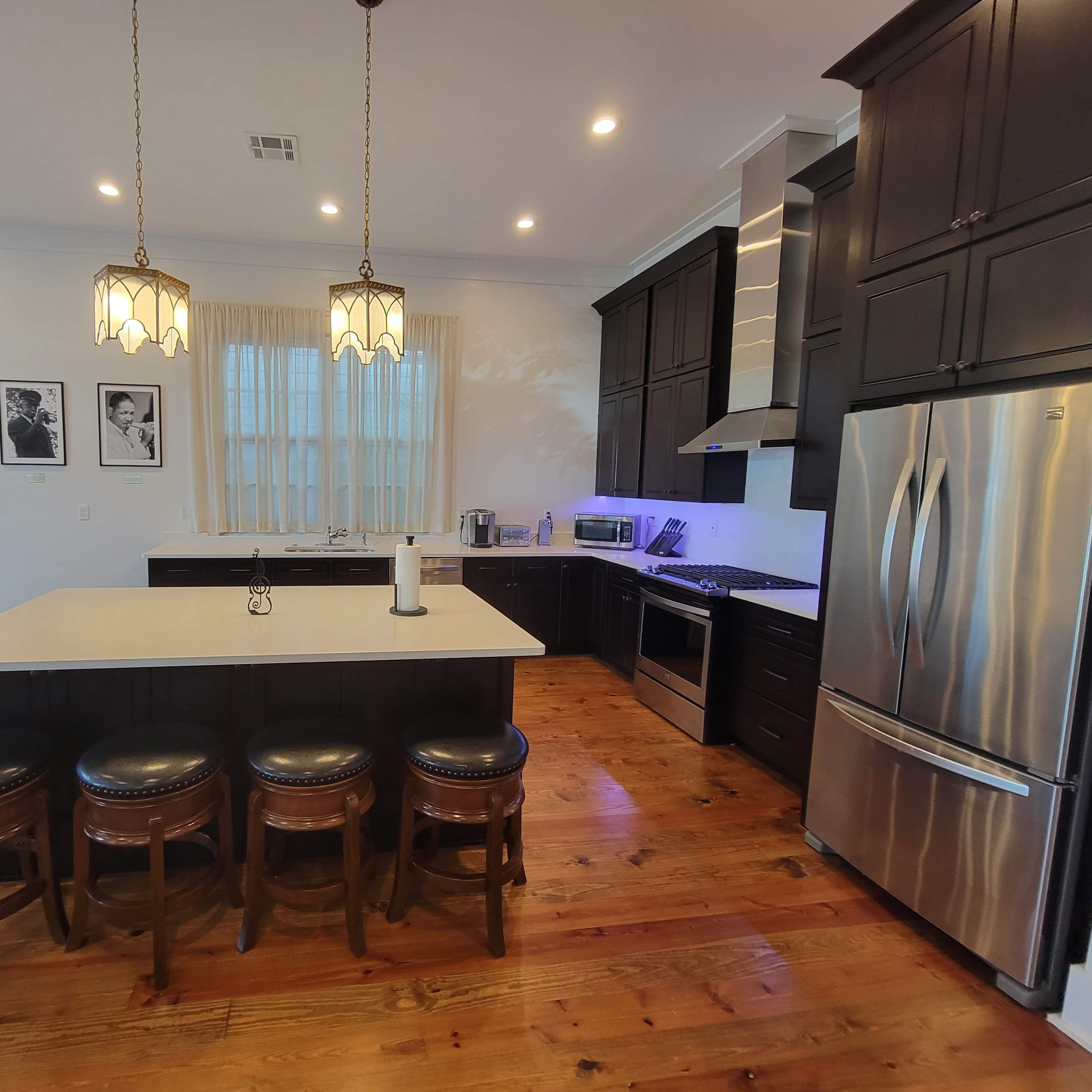 The kitchen features dark cabinetry, a large island with seating, stainless steel appliances, and pendant lighting.