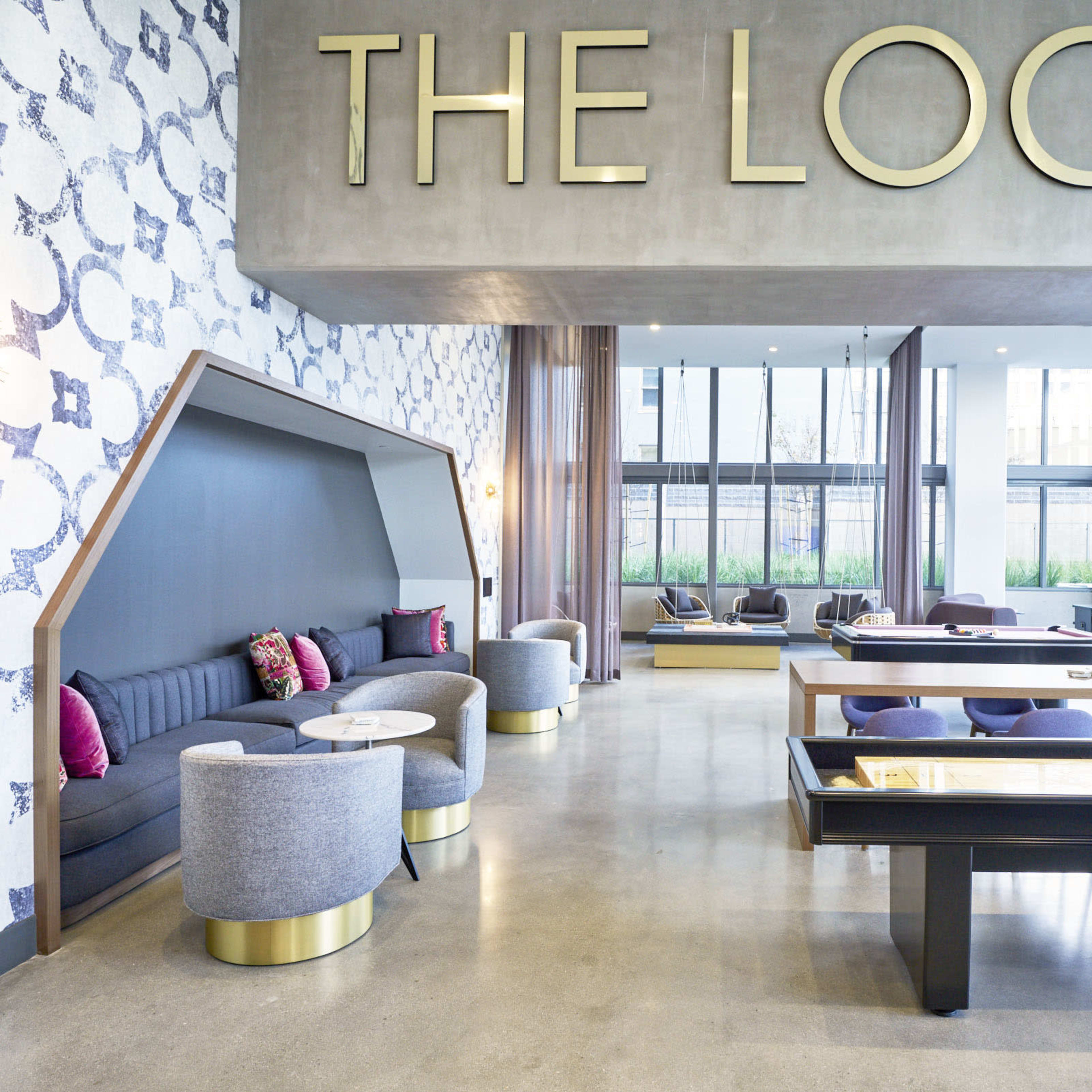 A modern lobby area with a large sign reading "THE LOCAL," featuring seating arrangements and large windows that allow natural light to enter.