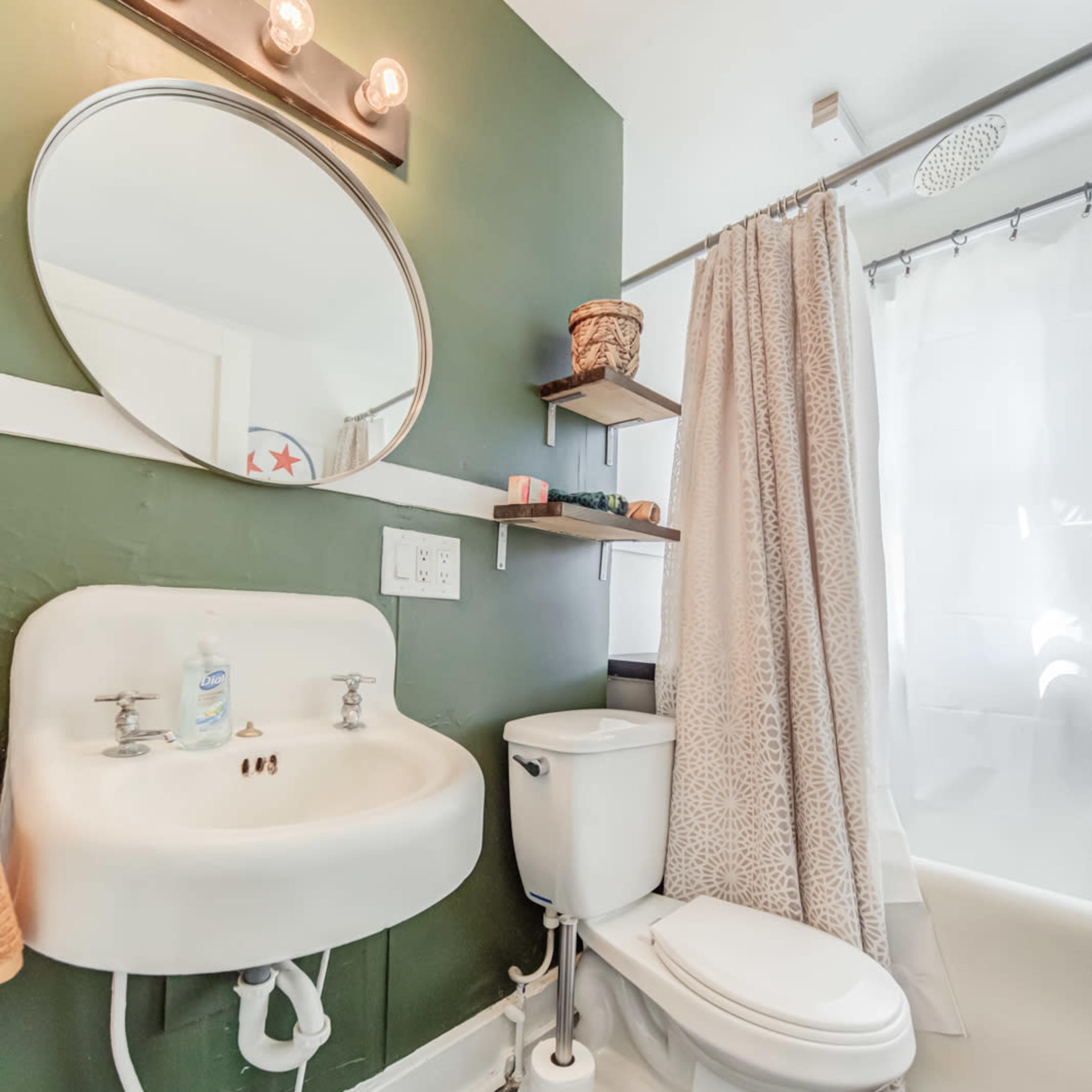 A small bathroom featuring a sink, a toilet, a mirror, and a shower with a curtain, all set against a dark green wall.