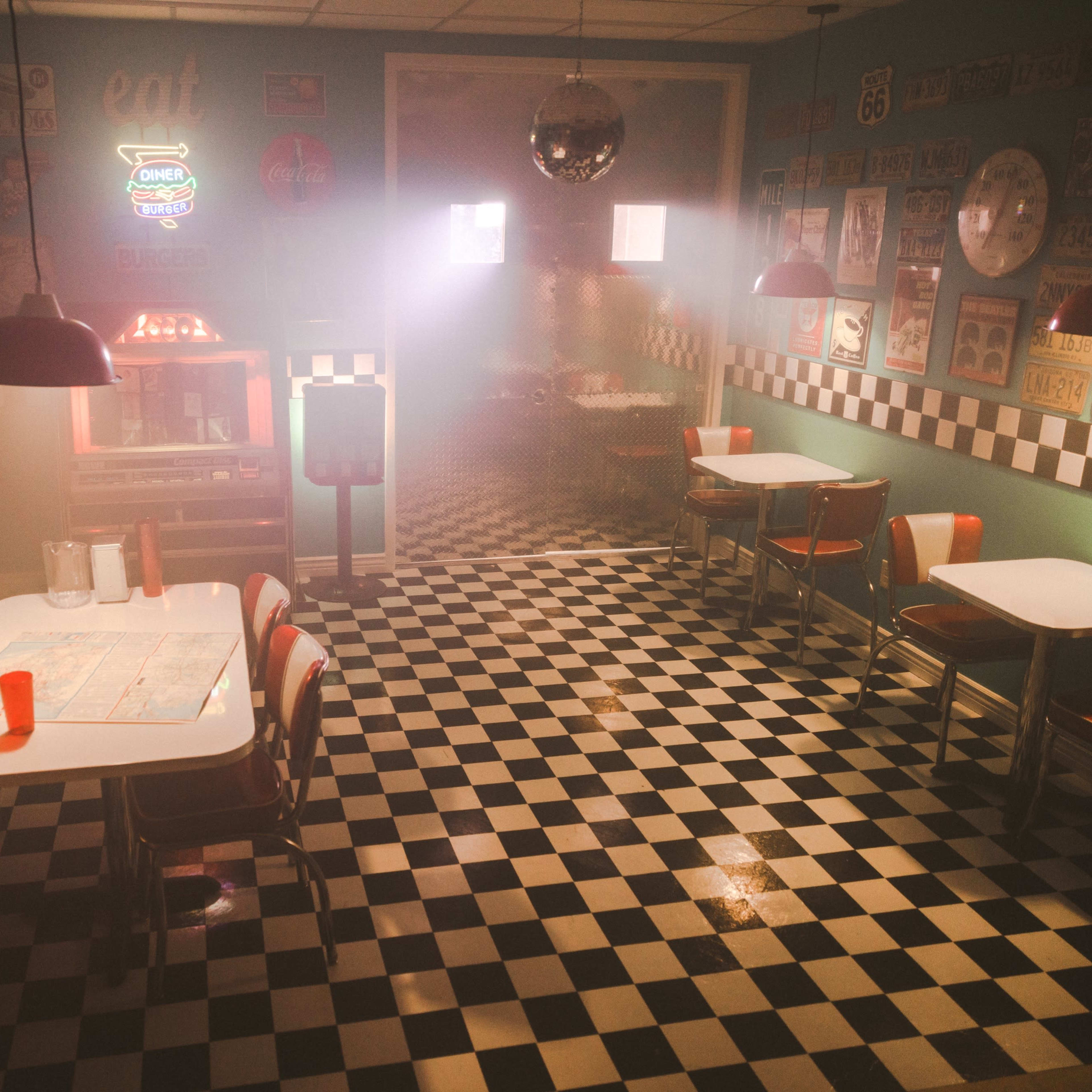 A retro diner with checkerboard floors, red vinyl booths, and dim lighting, featuring old signage on the walls.