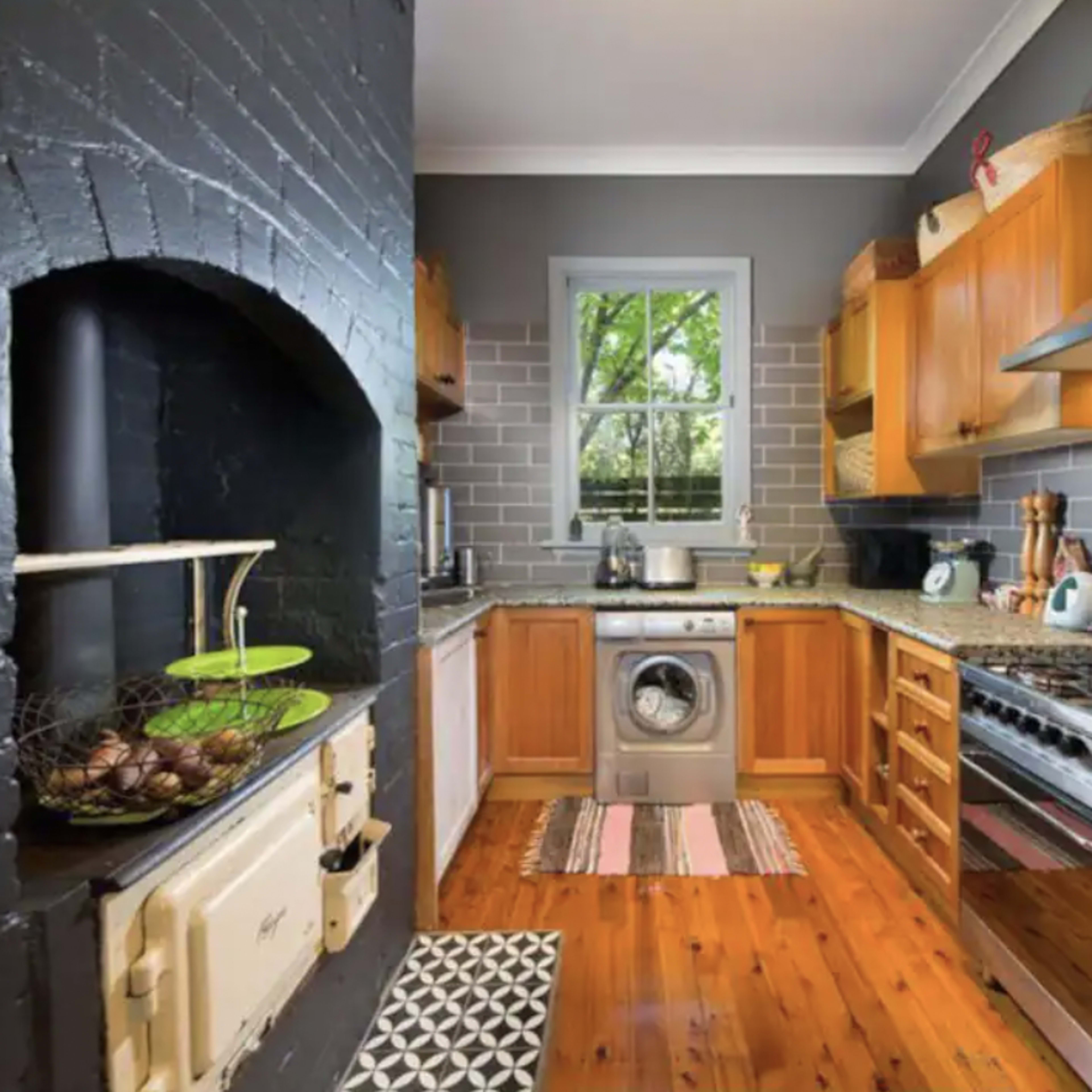The kitchen features wood cabinets, stainless steel appliances, a washing machine, and a combination of black and gray walls, with natural light coming through a window.