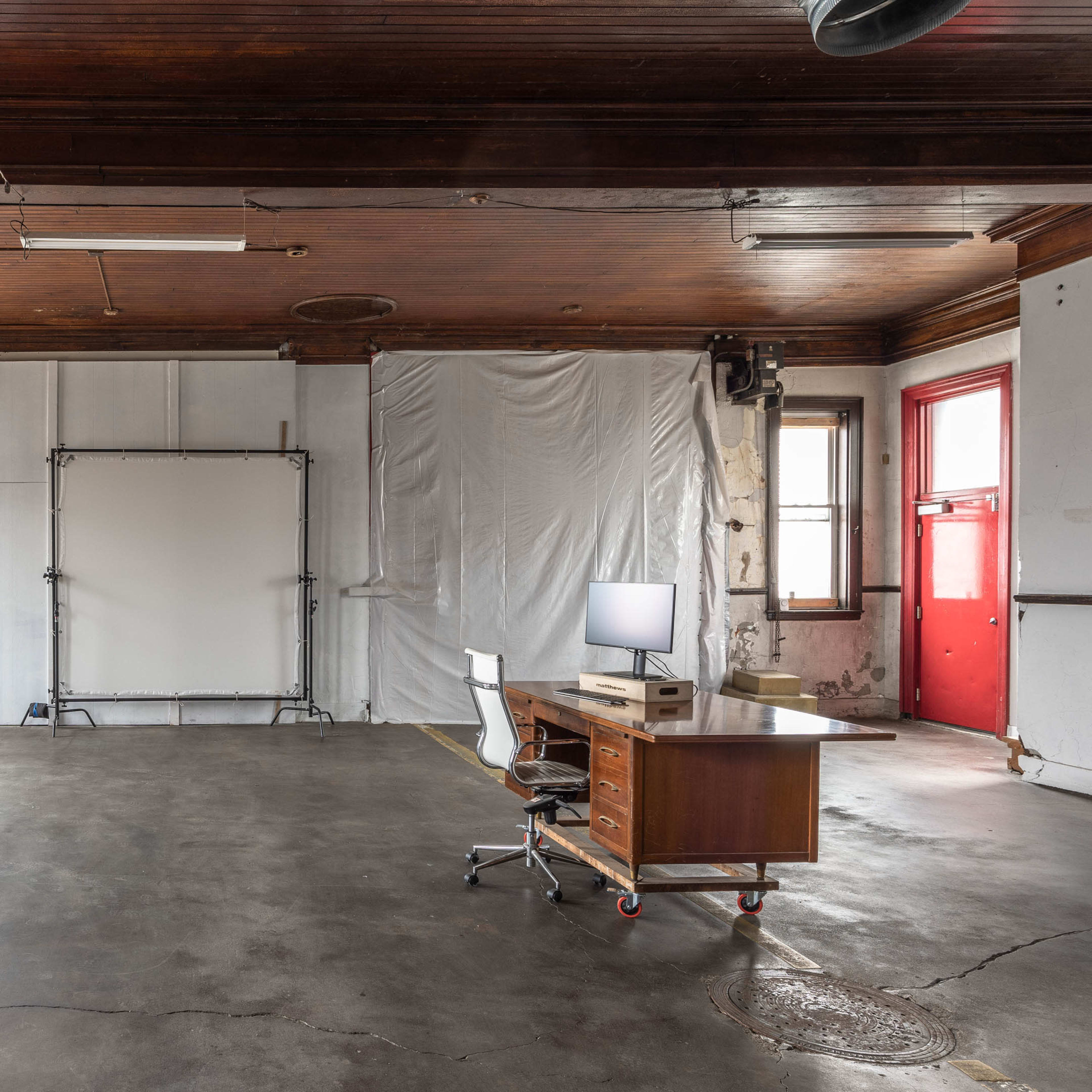 An empty room with a wooden ceiling, a metal desk with a chair, and a backdrop setup against one wall.