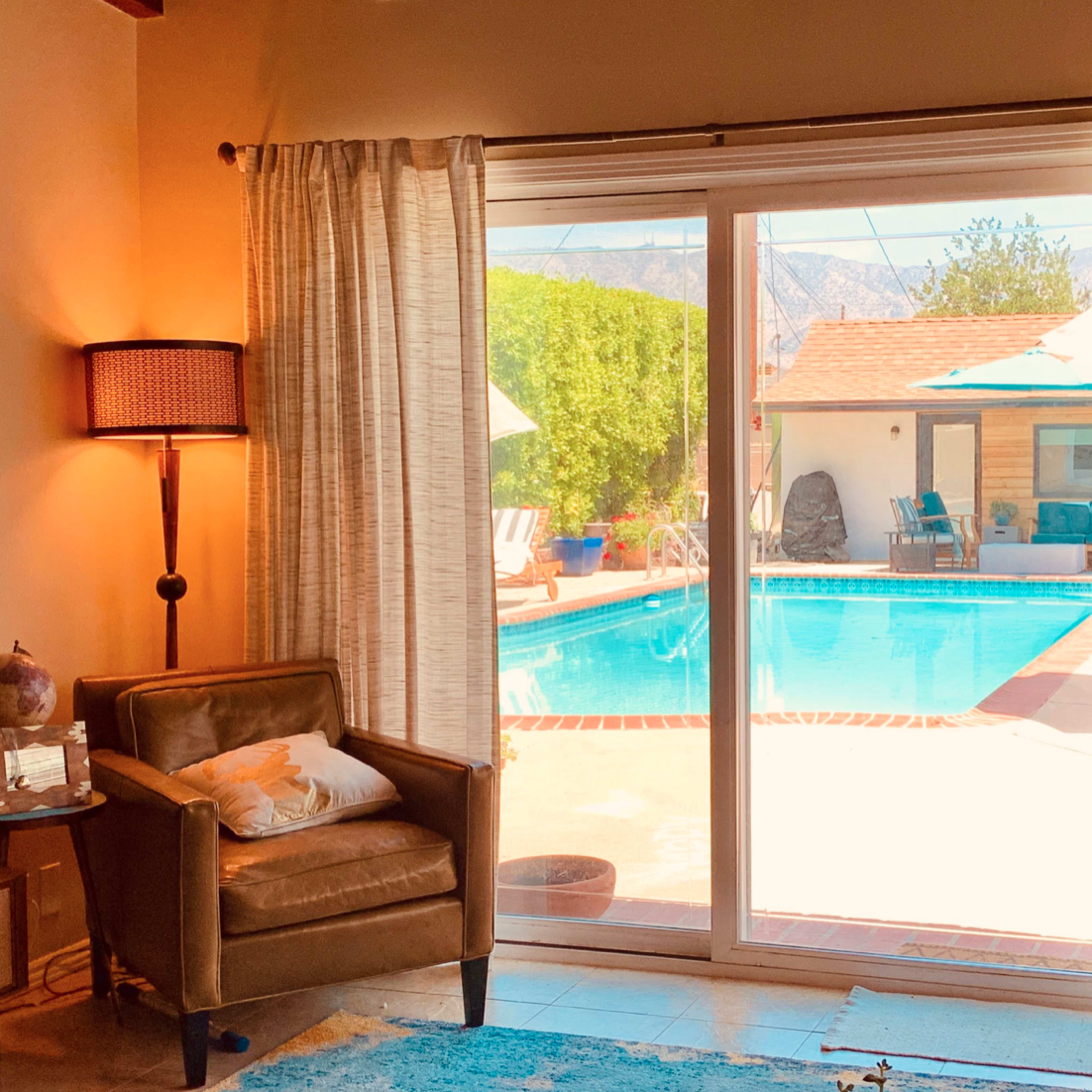 A living room with a tan armchair and a view of a swimming pool through large glass doors.