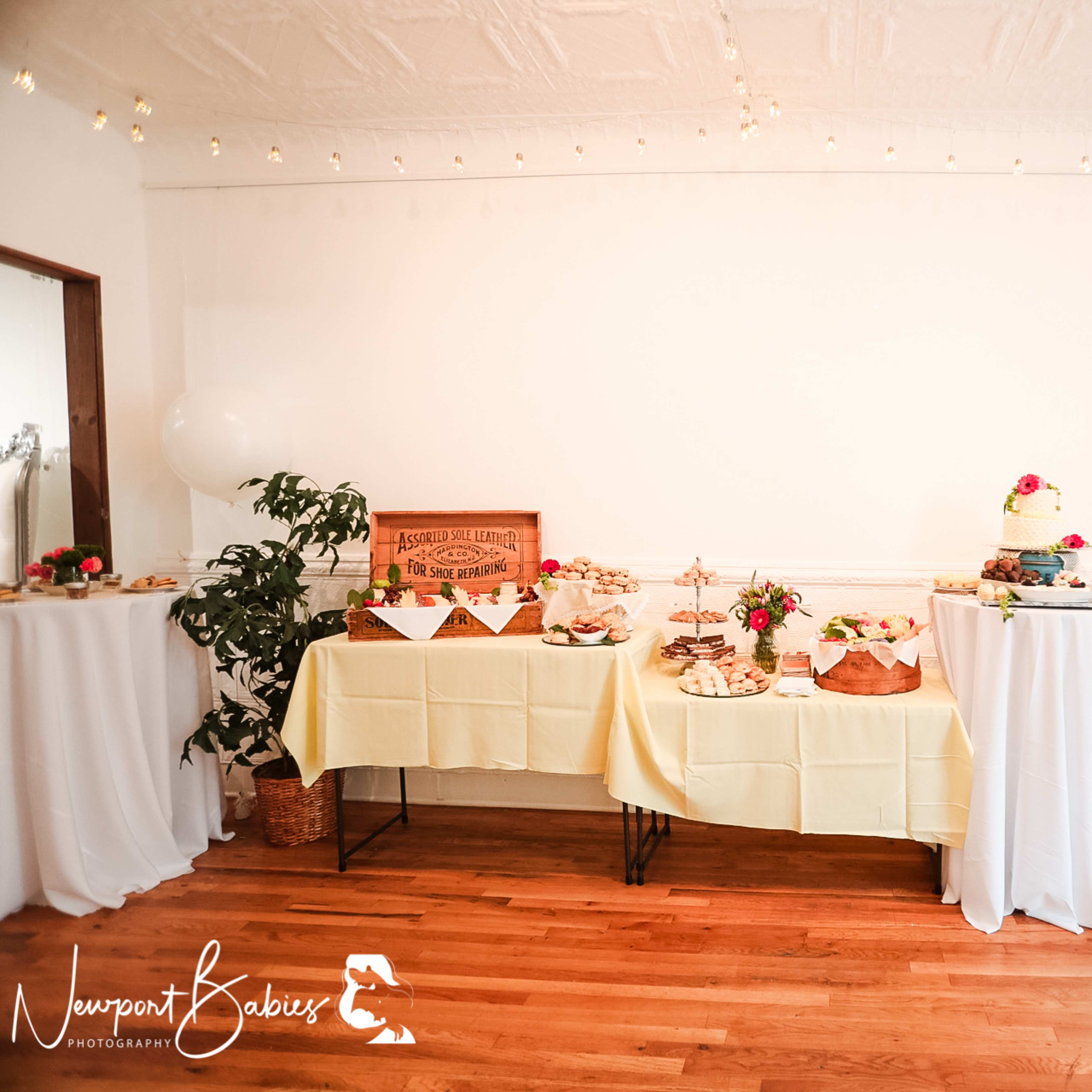 A table adorned with a yellow tablecloth displays an array of desserts and snacks, complemented by floral arrangements and decorative items, in a well-lit room.