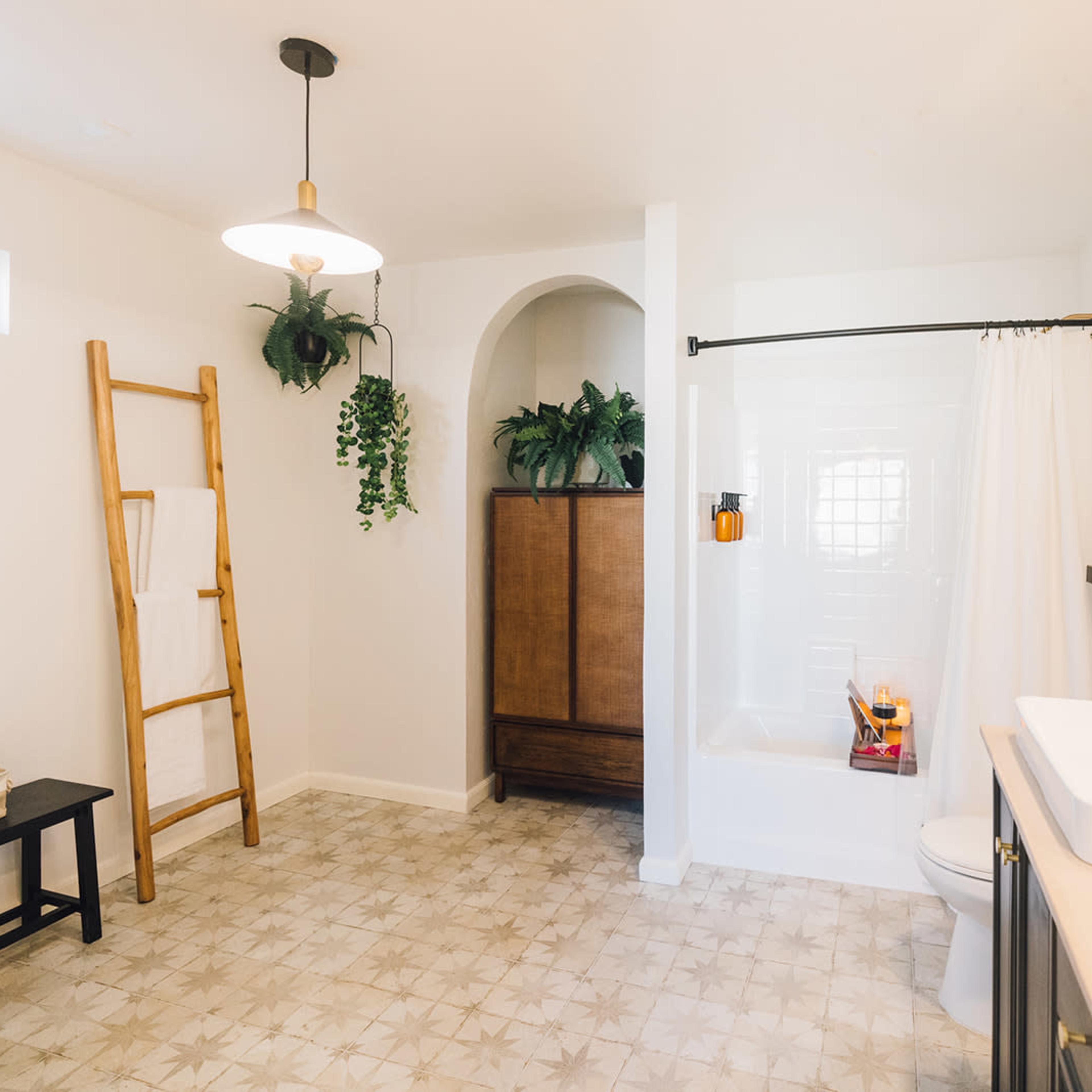 A clean and modern bathroom featuring a bathtub, a wooden cabinet, a hanging towel ladder, and plants integrated into the decor.