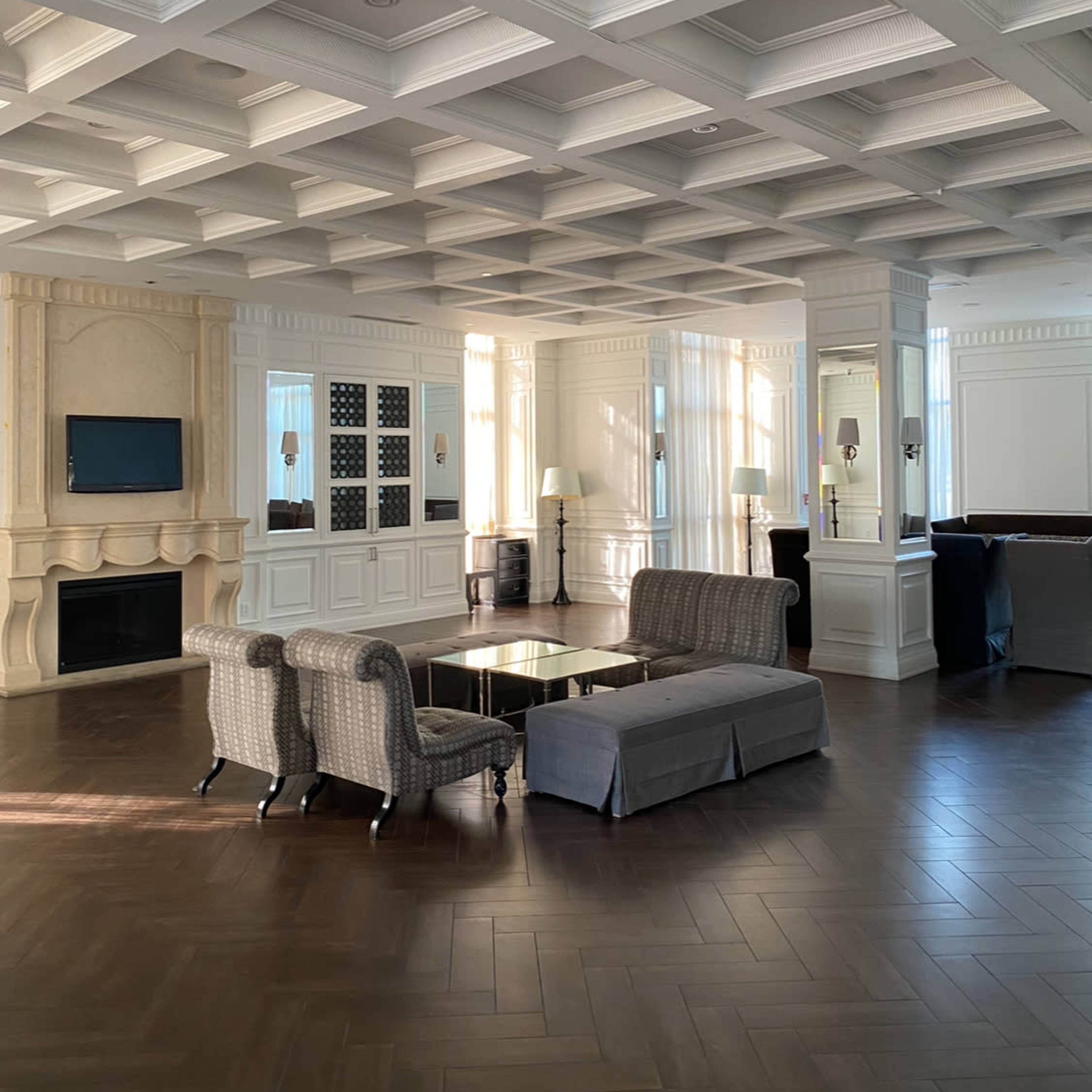 A spacious living room with coffered ceilings, elegant furniture, and natural light filtering through large windows.