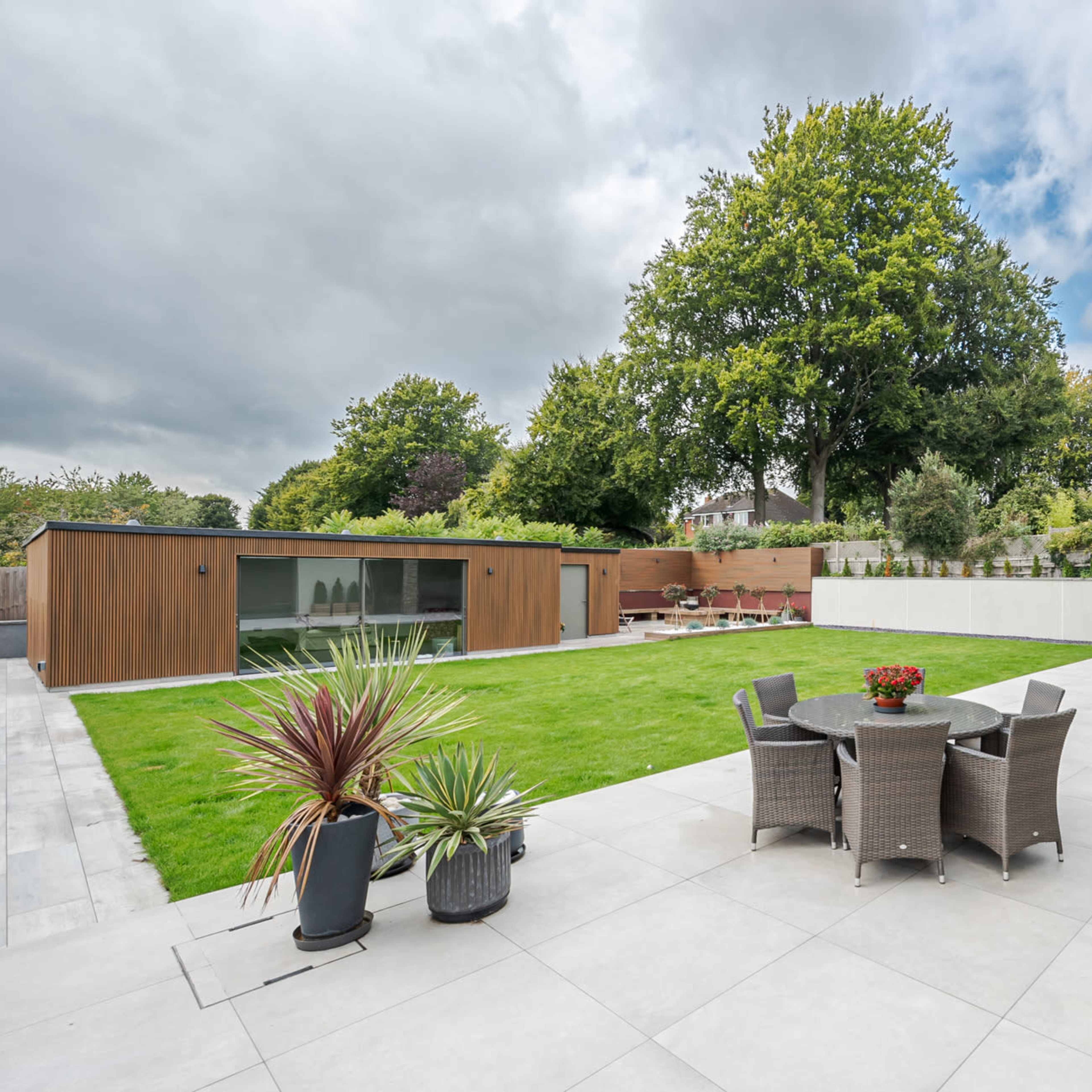 A modern backyard features a patio with dining furniture, a manicured lawn, and a contemporary shed among landscaped greenery.