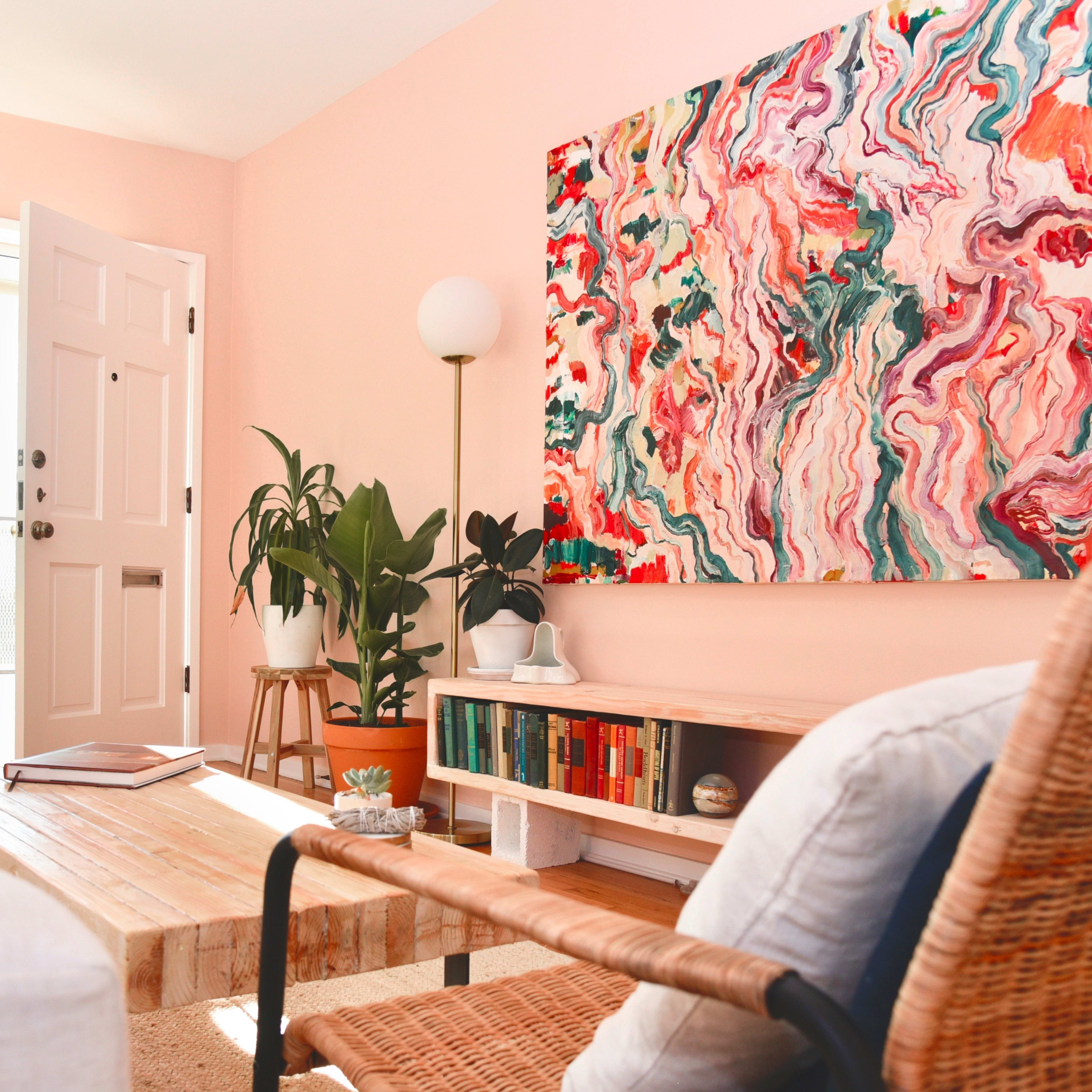 A bright living room features a large abstract painting on the wall, potted plants, a wooden coffee table, and comfortable seating.