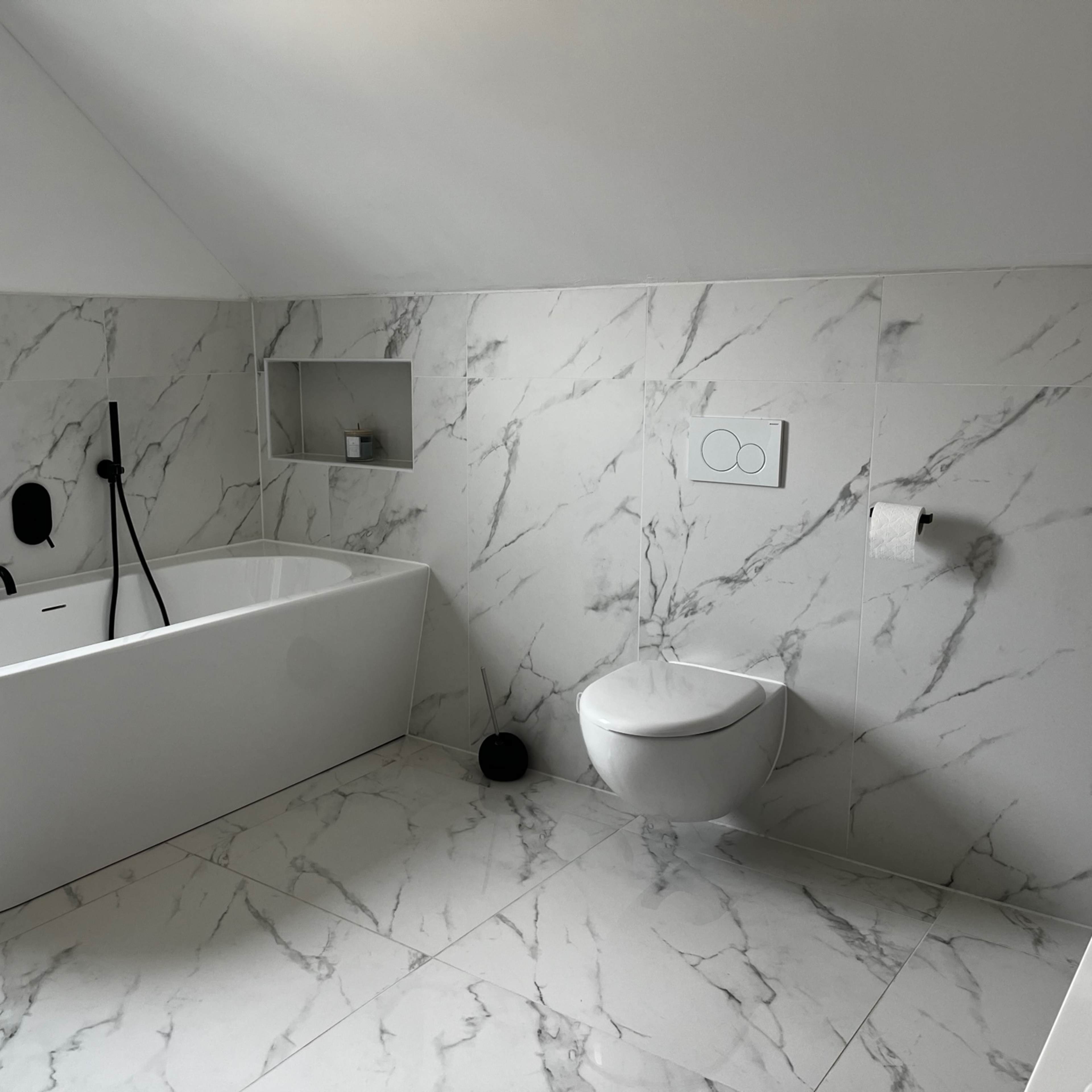 A modern bathroom featuring a freestanding bathtub, a wall-mounted toilet, and marble-patterned tiled walls and floor.