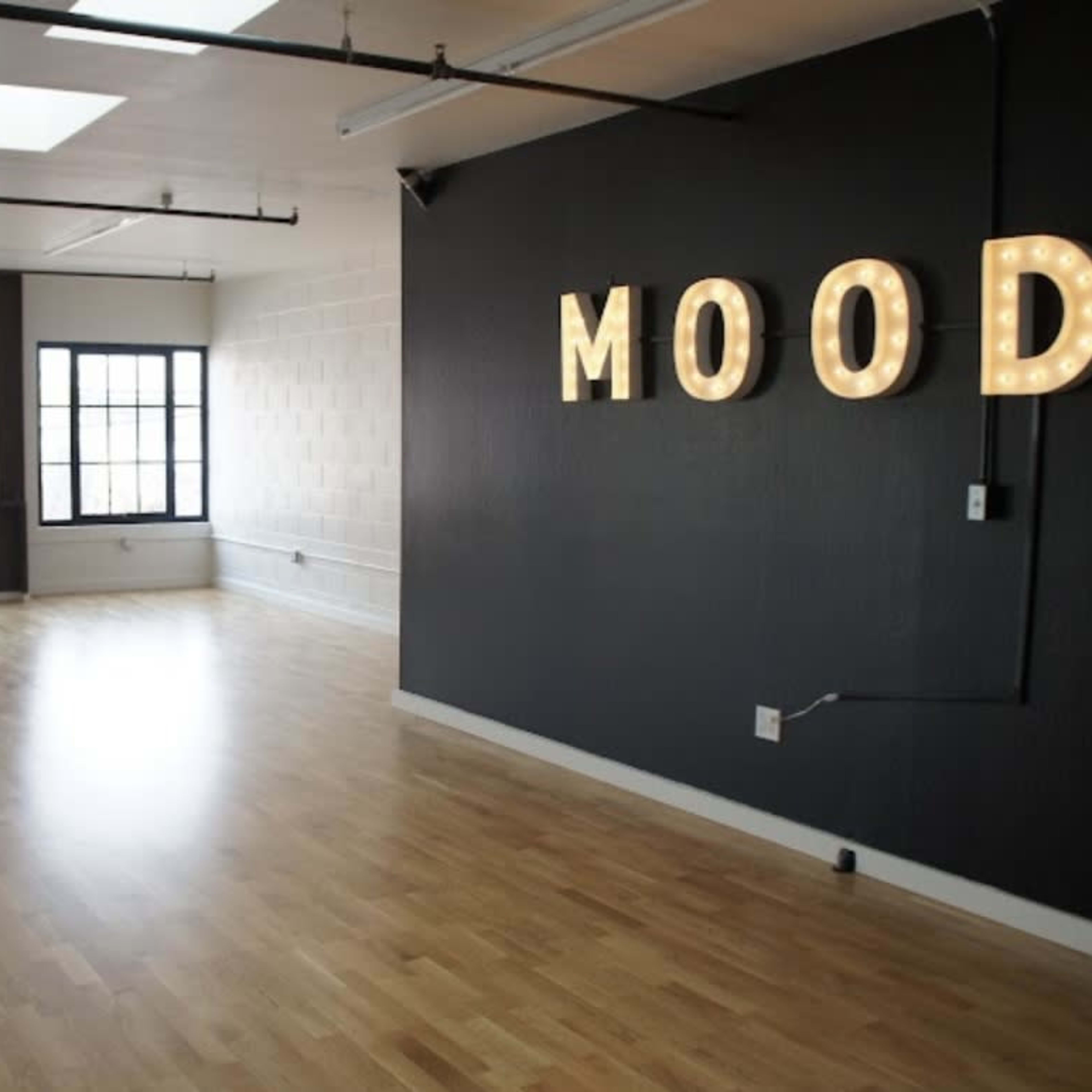 A spacious room features large windows and a dark wall with lit letters spelling "MOOD."