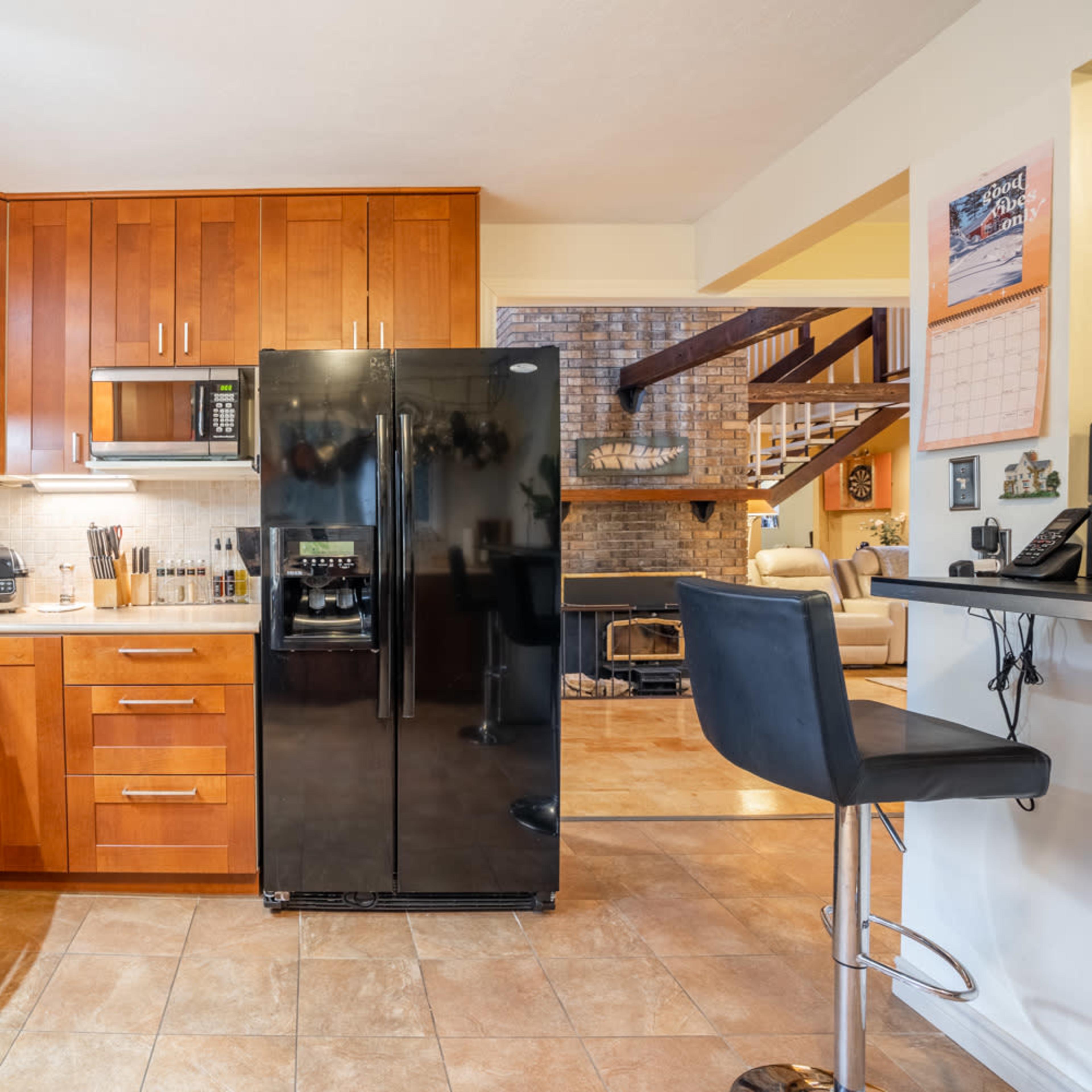 A kitchen with wooden cabinets, a black refrigerator, stainless steel appliances, and a tile floor.