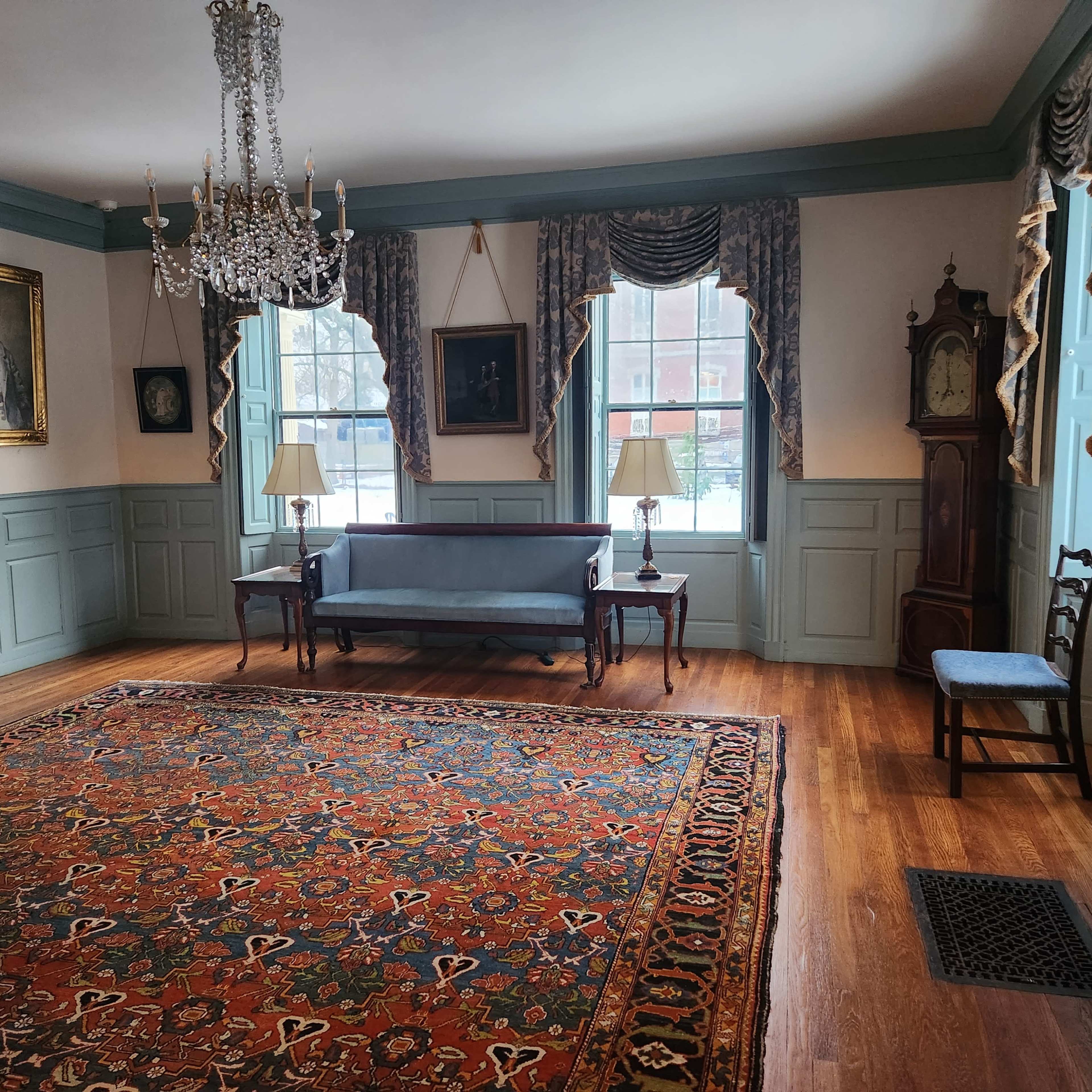 The room features a blue sofa, two lamps, a large area rug, and various framed artworks on the walls.