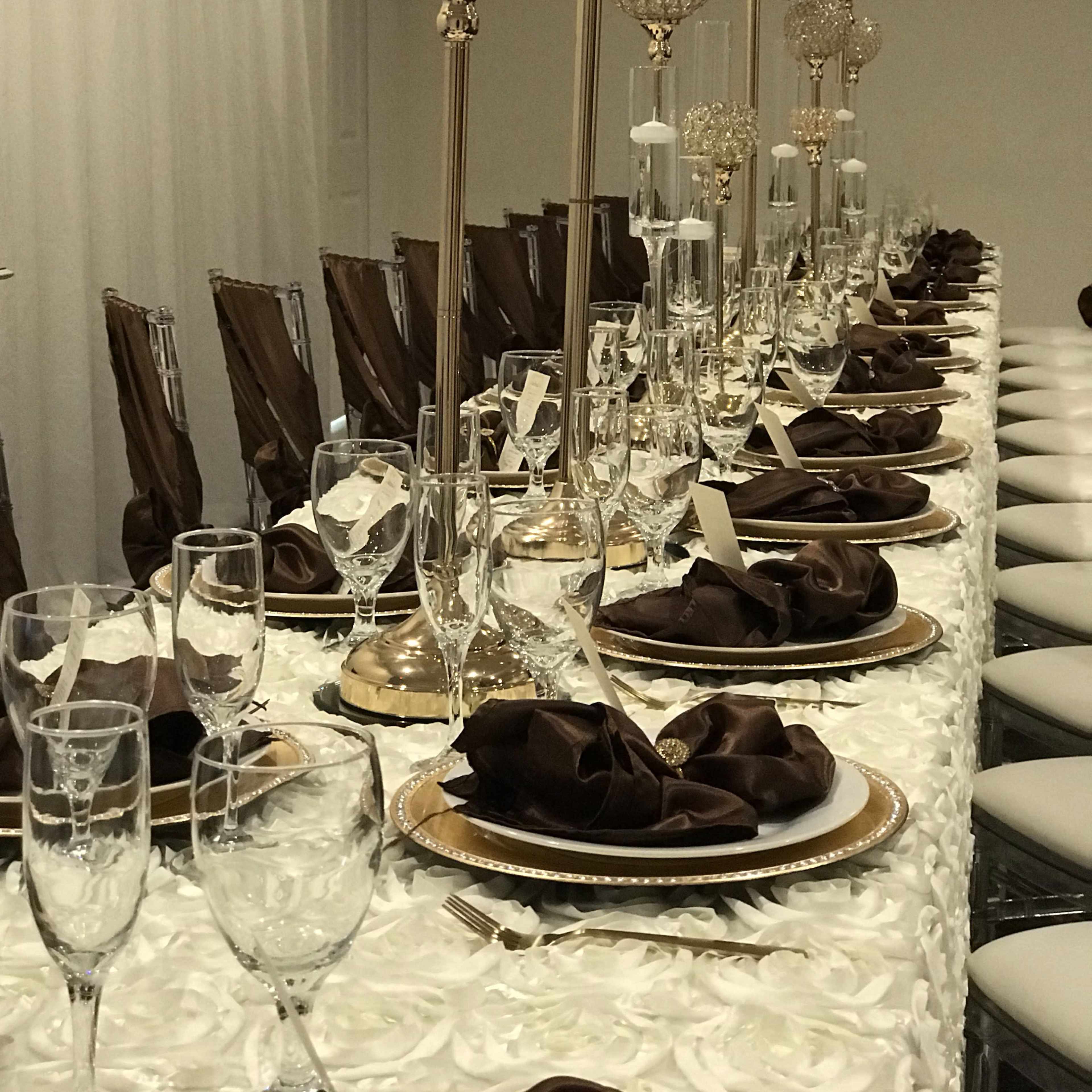 A long dining table is elegantly set with gold and crystal centerpieces, brown napkins, and fine glassware.
