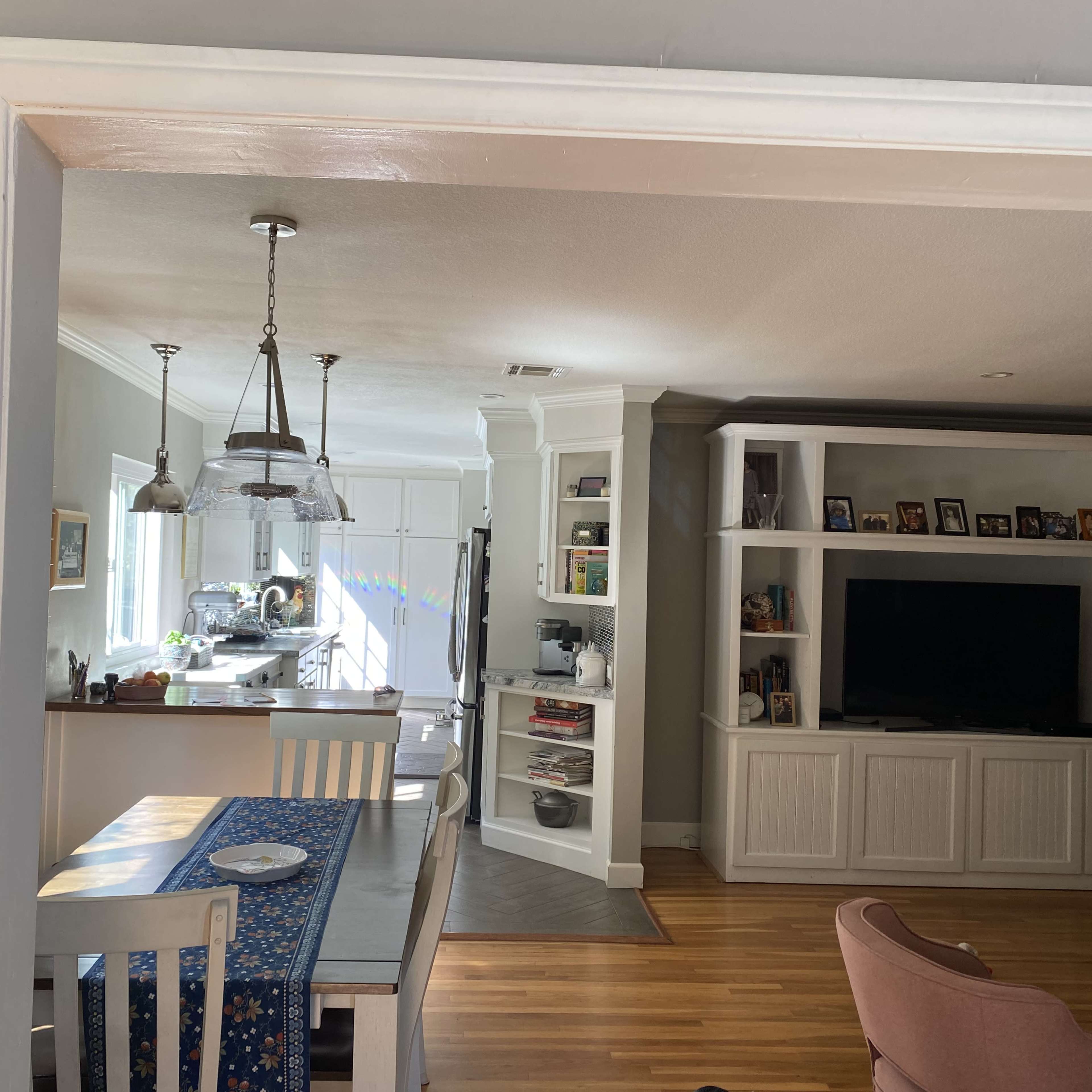 A home interior where a dining area with a table is visible through an archway, leading to a living area with built-in shelves and a television.