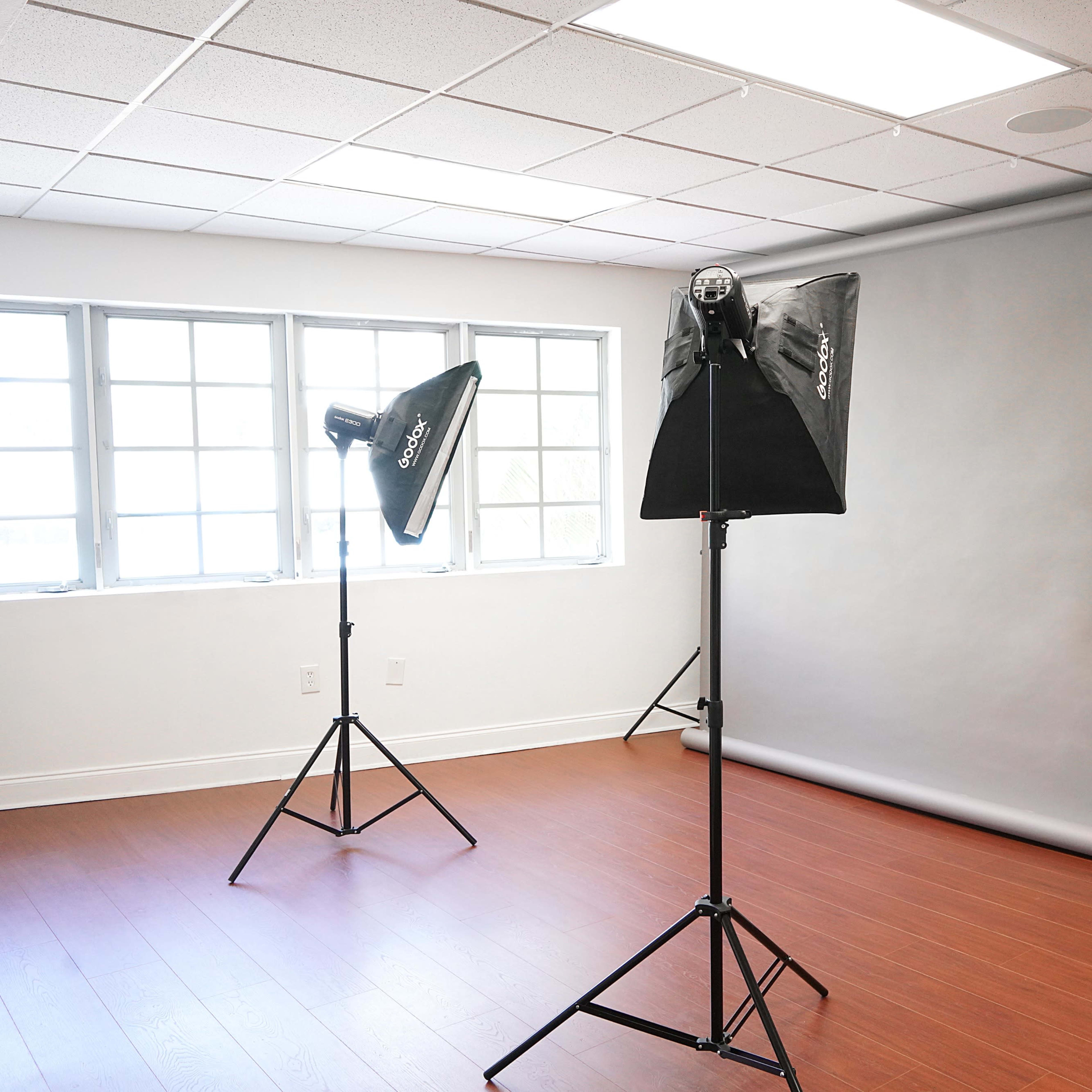 A photography studio with two softbox lights positioned on stands and a gray backdrop set up against the wall.