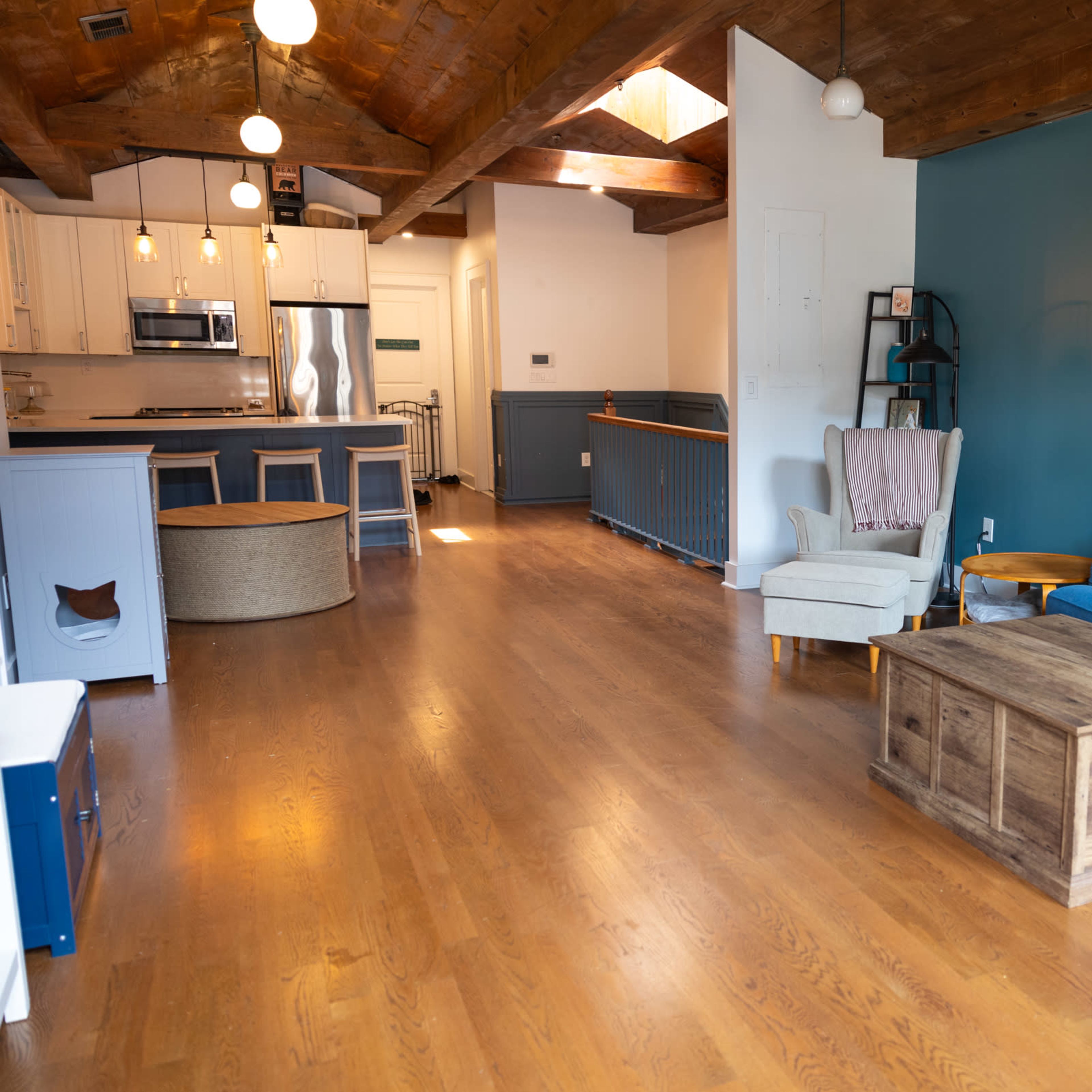 A spacious living area featuring a blue couch, a wooden coffee table, and an open kitchen area with white cabinetry and stainless steel appliances.