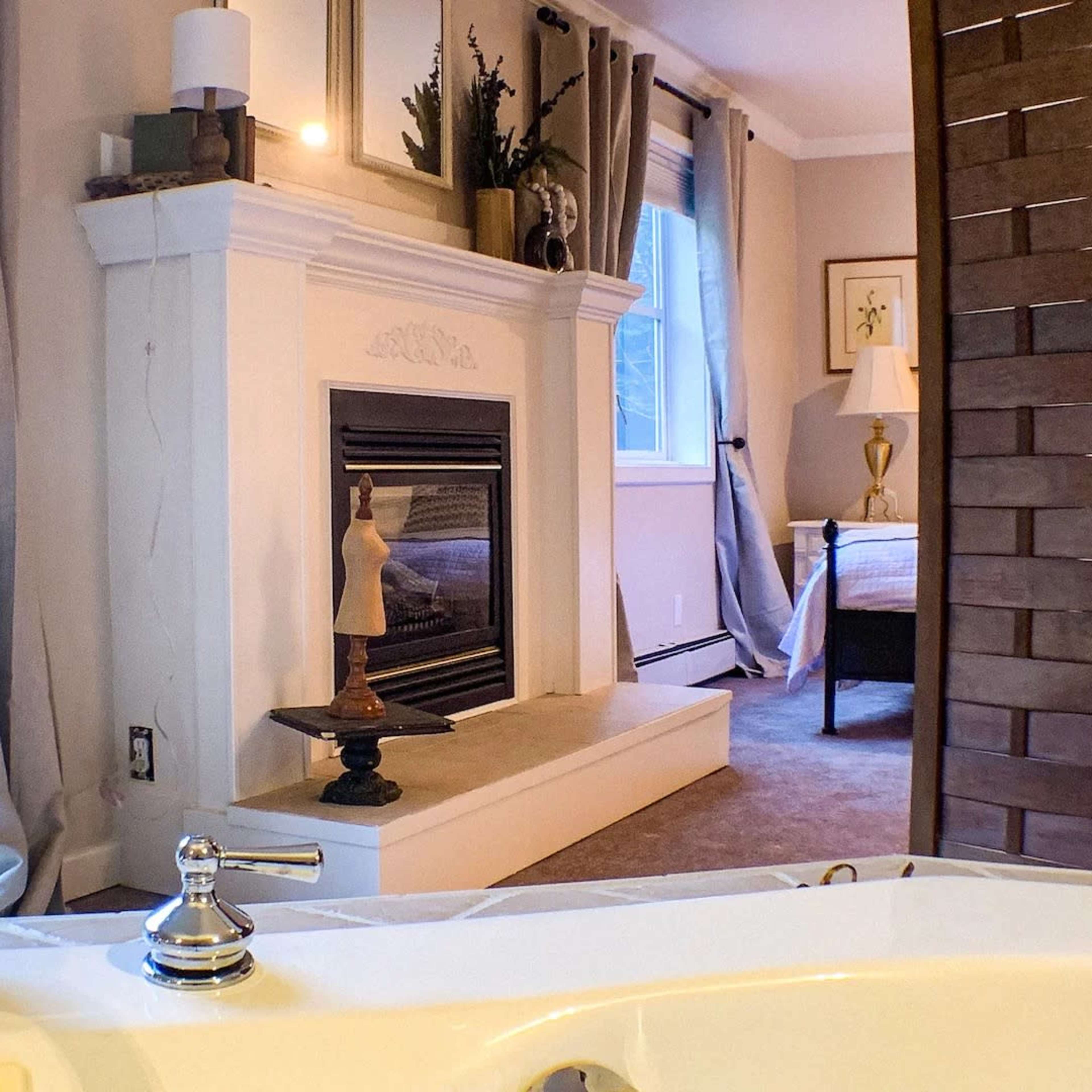 A bathroom with a view of a cozy bedroom and a fireplace, framed by curtains and a wooden partition.