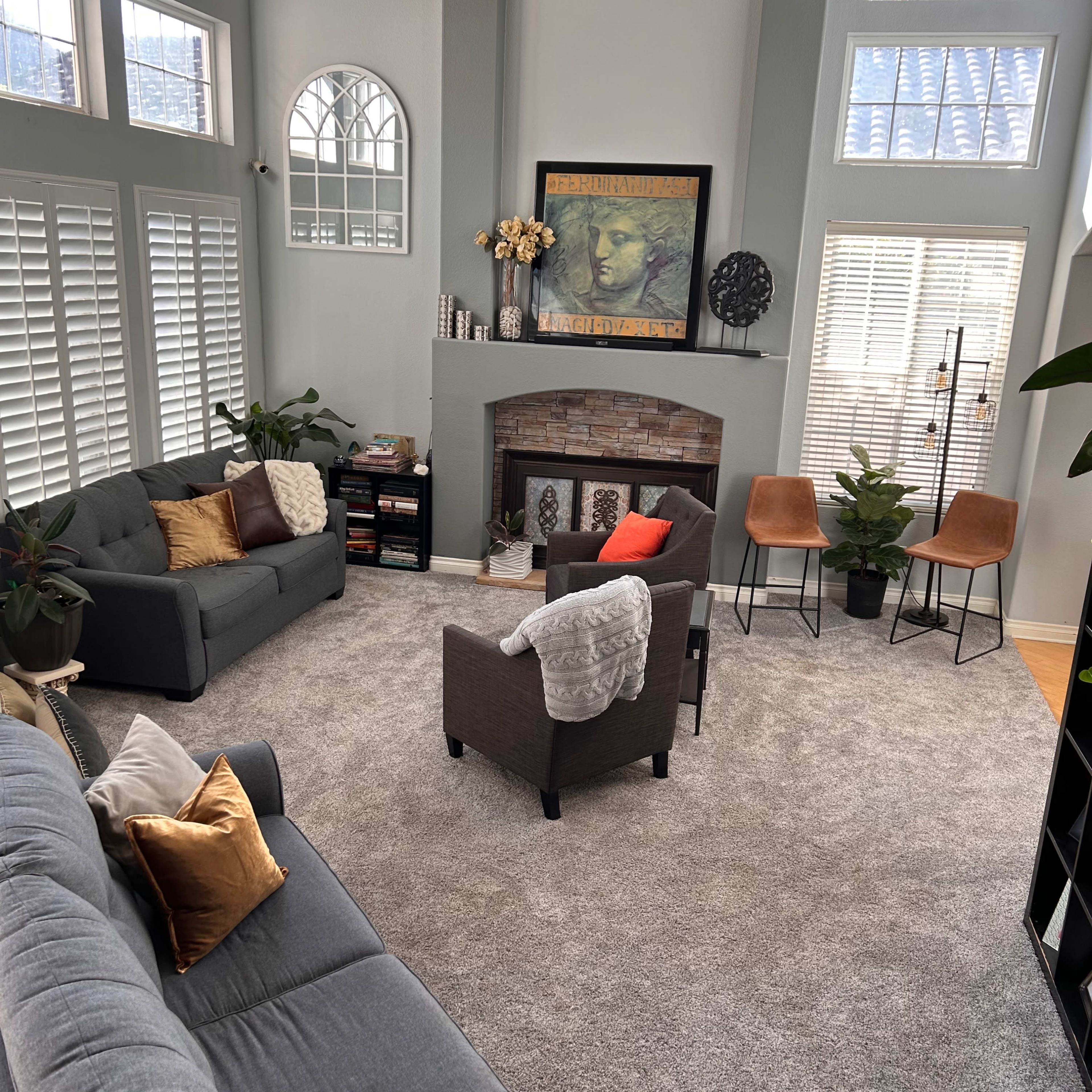 A spacious living room with two sofas, a fireplace, decorative plants, and large windows allowing natural light to fill the area.