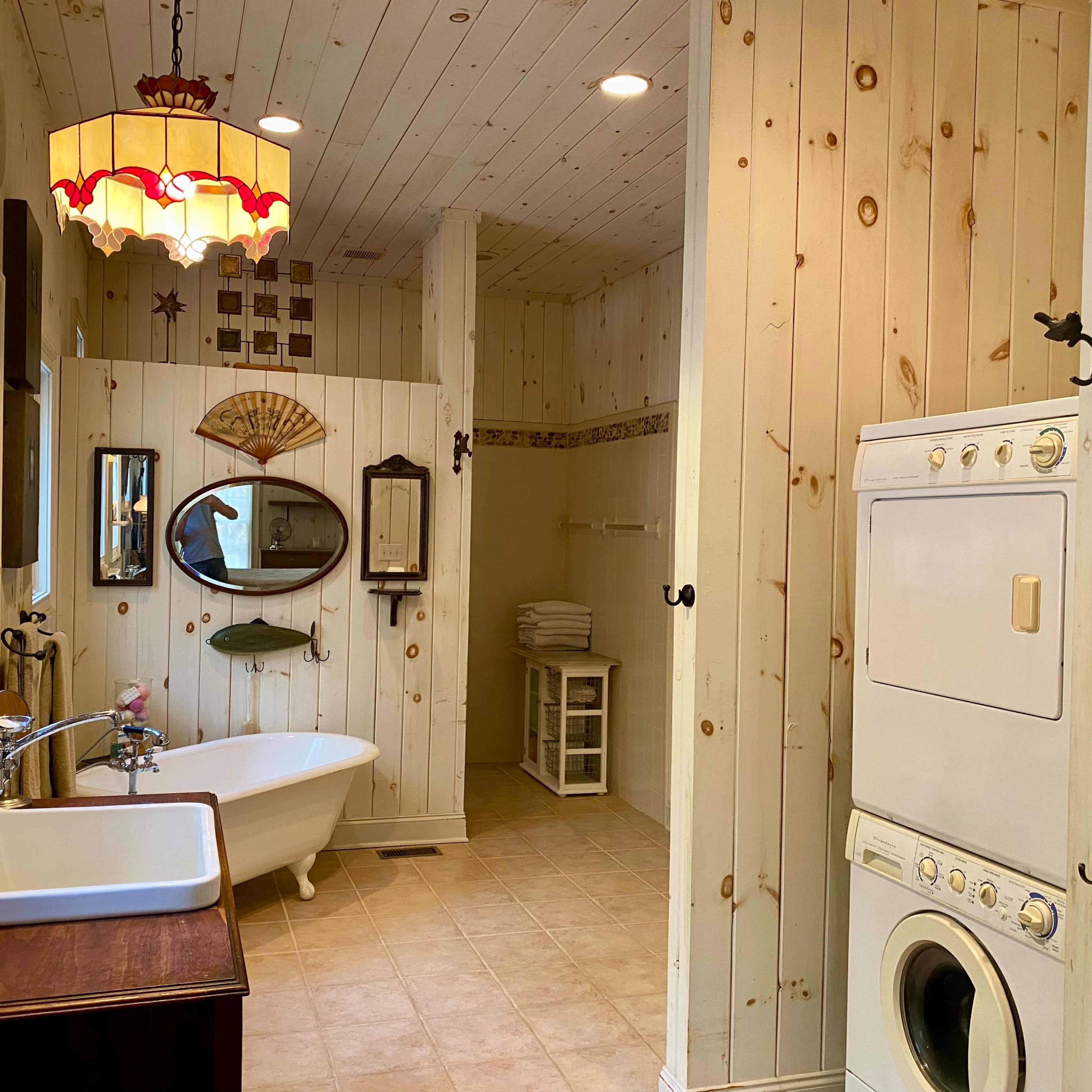 A bathroom with a freestanding bathtub, a washing machine, and wooden paneling on the walls.