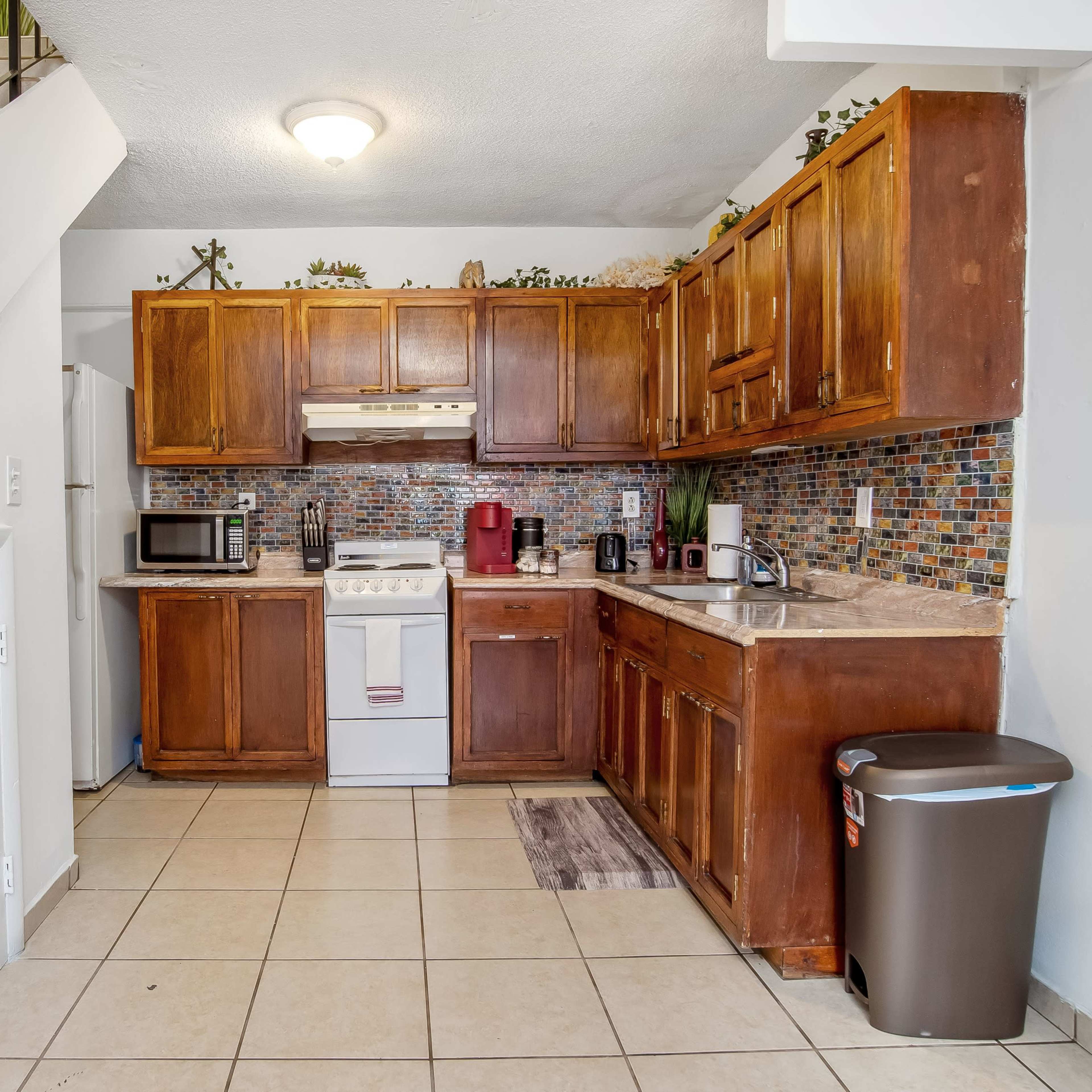 A compact kitchen features wooden cabinets, a gas stove, and a tiled backsplash, adjacent to a staircase with a white railing.