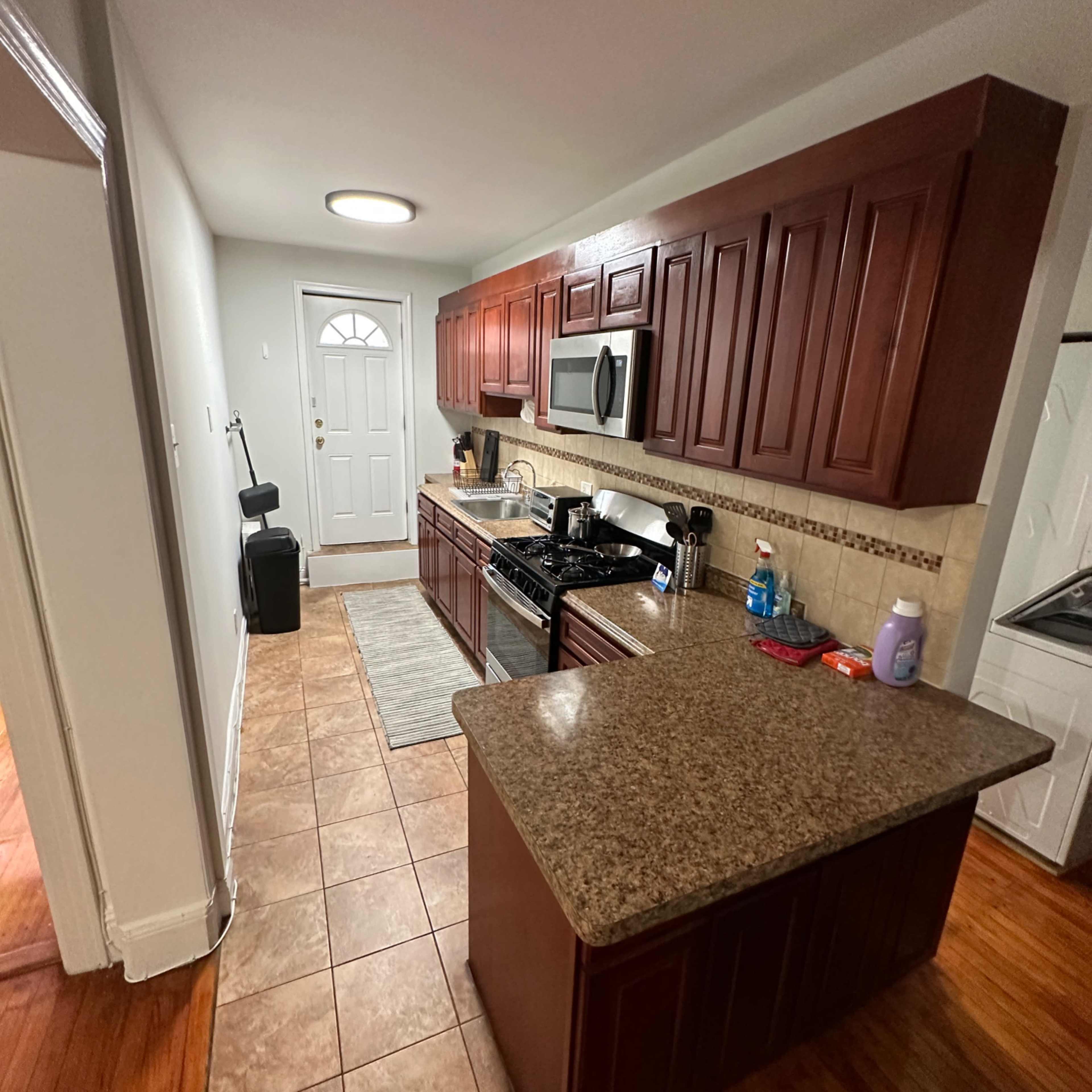 A kitchen with wooden cabinetry, a granite countertop, and appliances, adjacent to a front door.