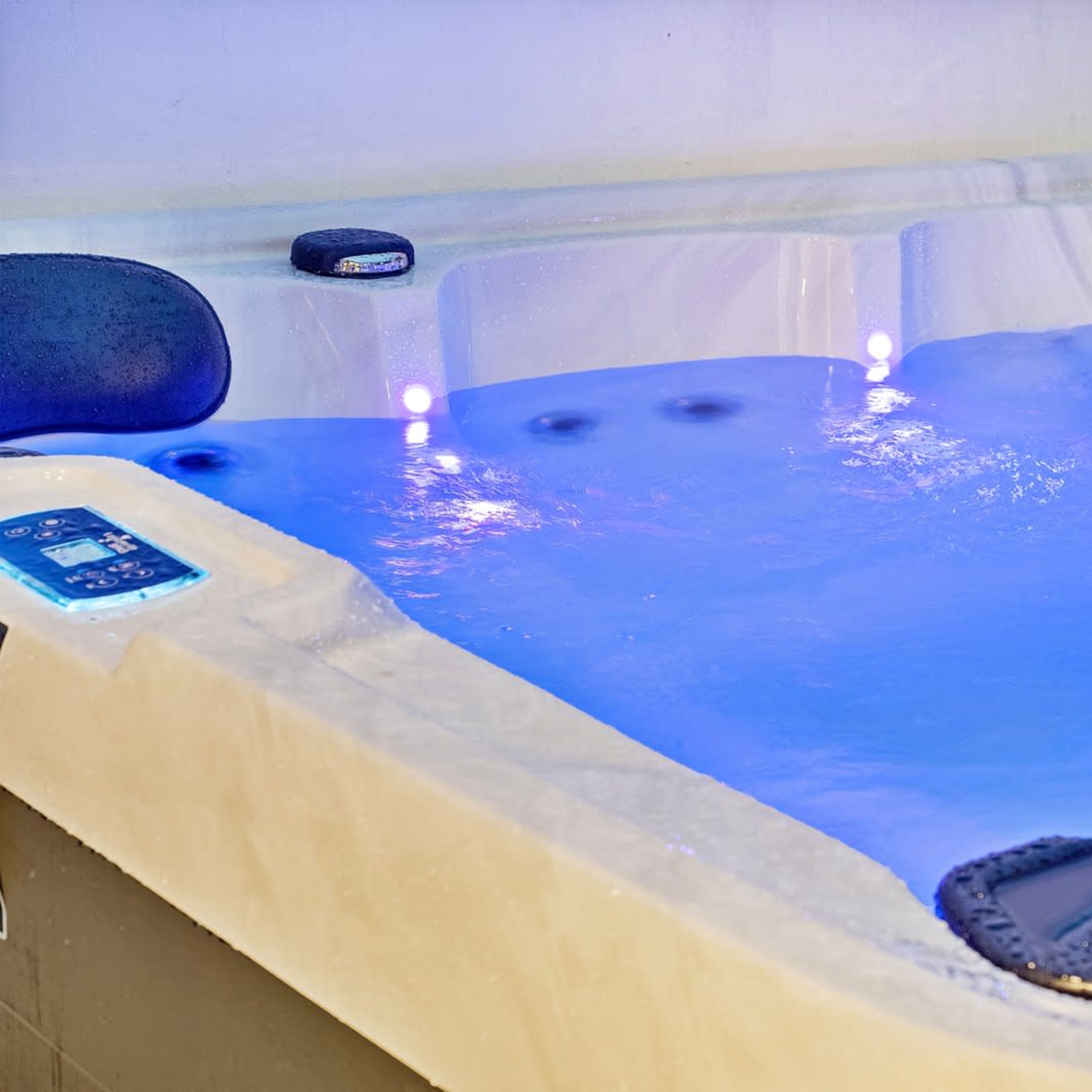 A hot tub with glowing blue water and built-in seating is filled with bubbles and illuminated by LED lights.