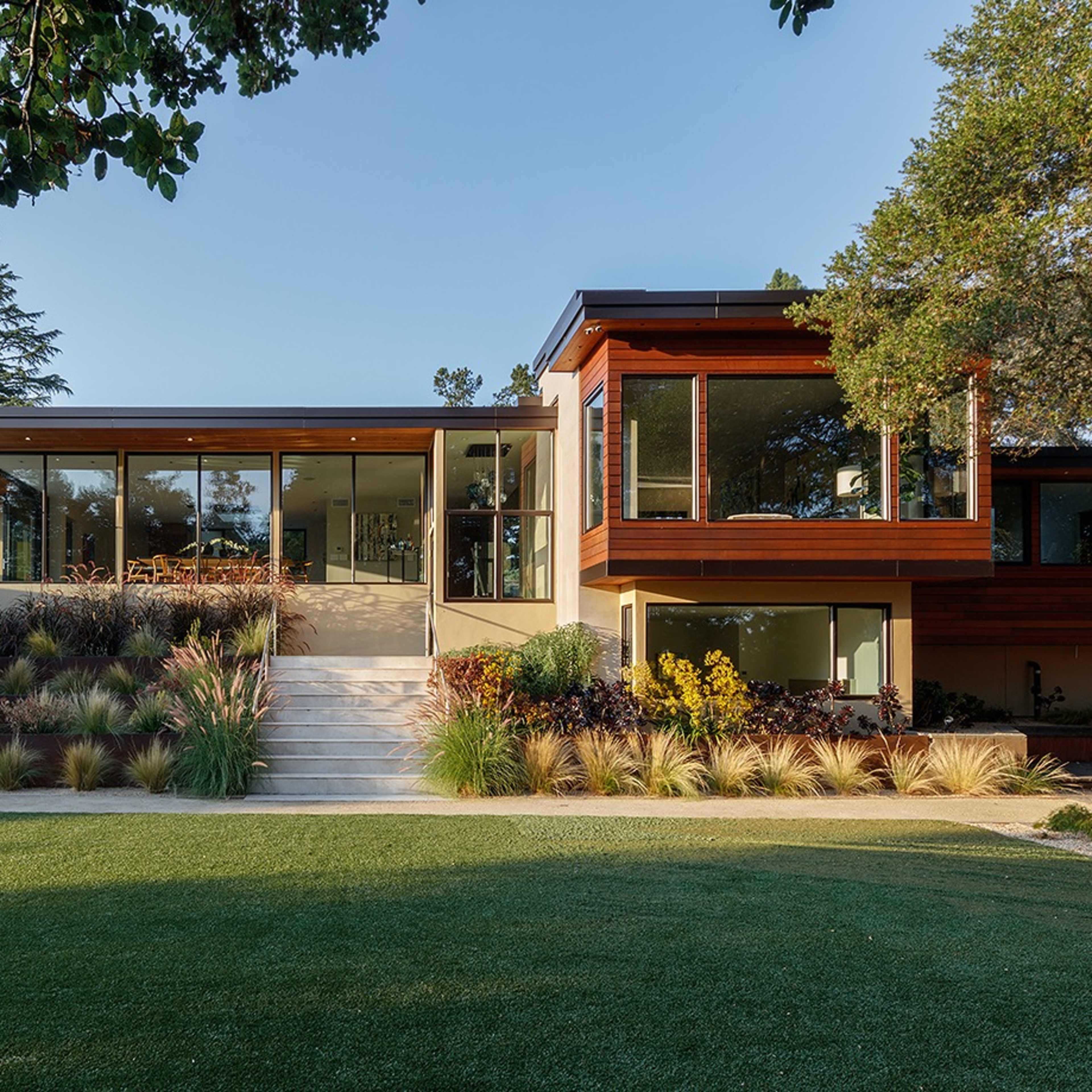 A modern house with large glass windows surrounded by landscaped greenery and a patio area.