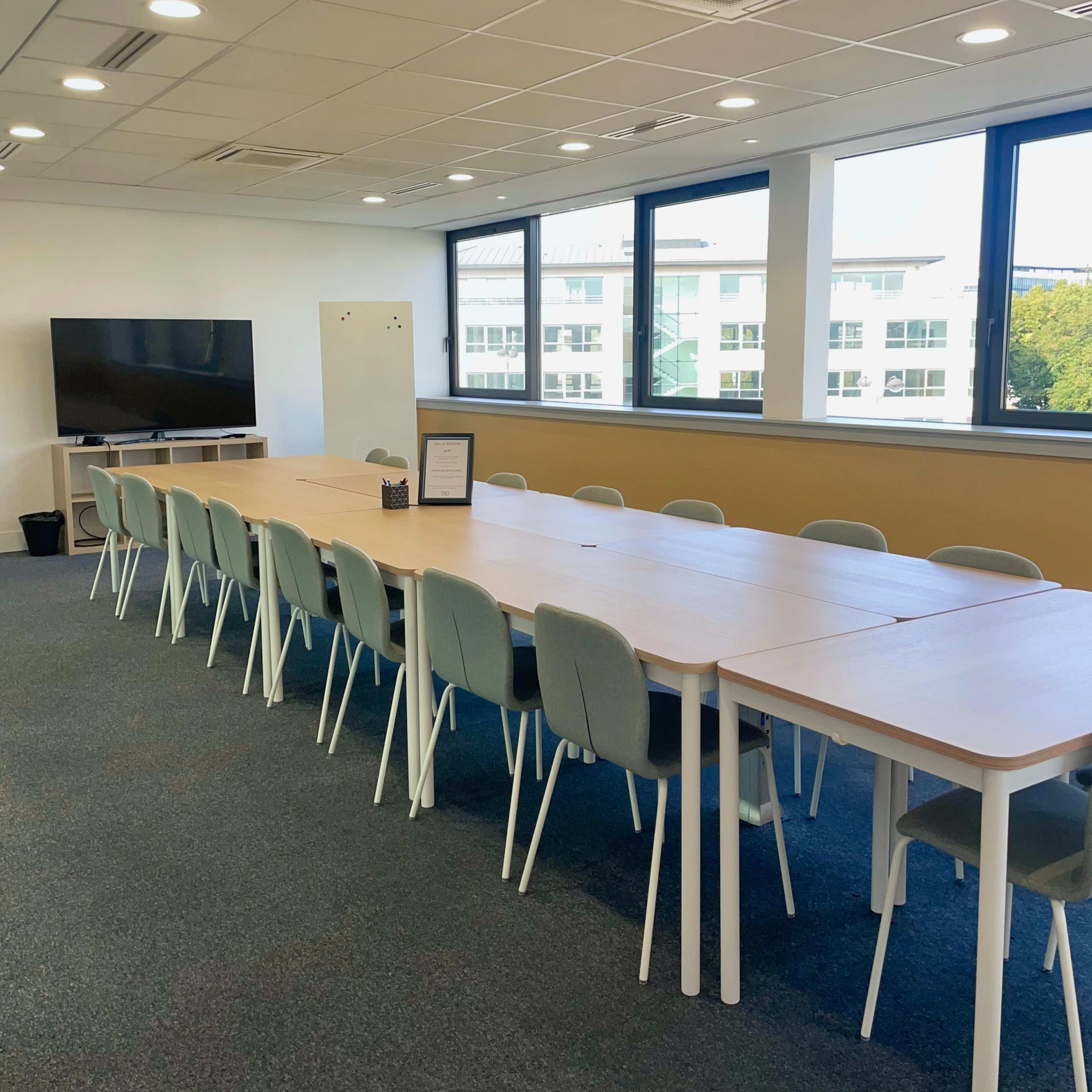 A large, modern meeting room features a long table with multiple chairs and a television mounted on the wall.