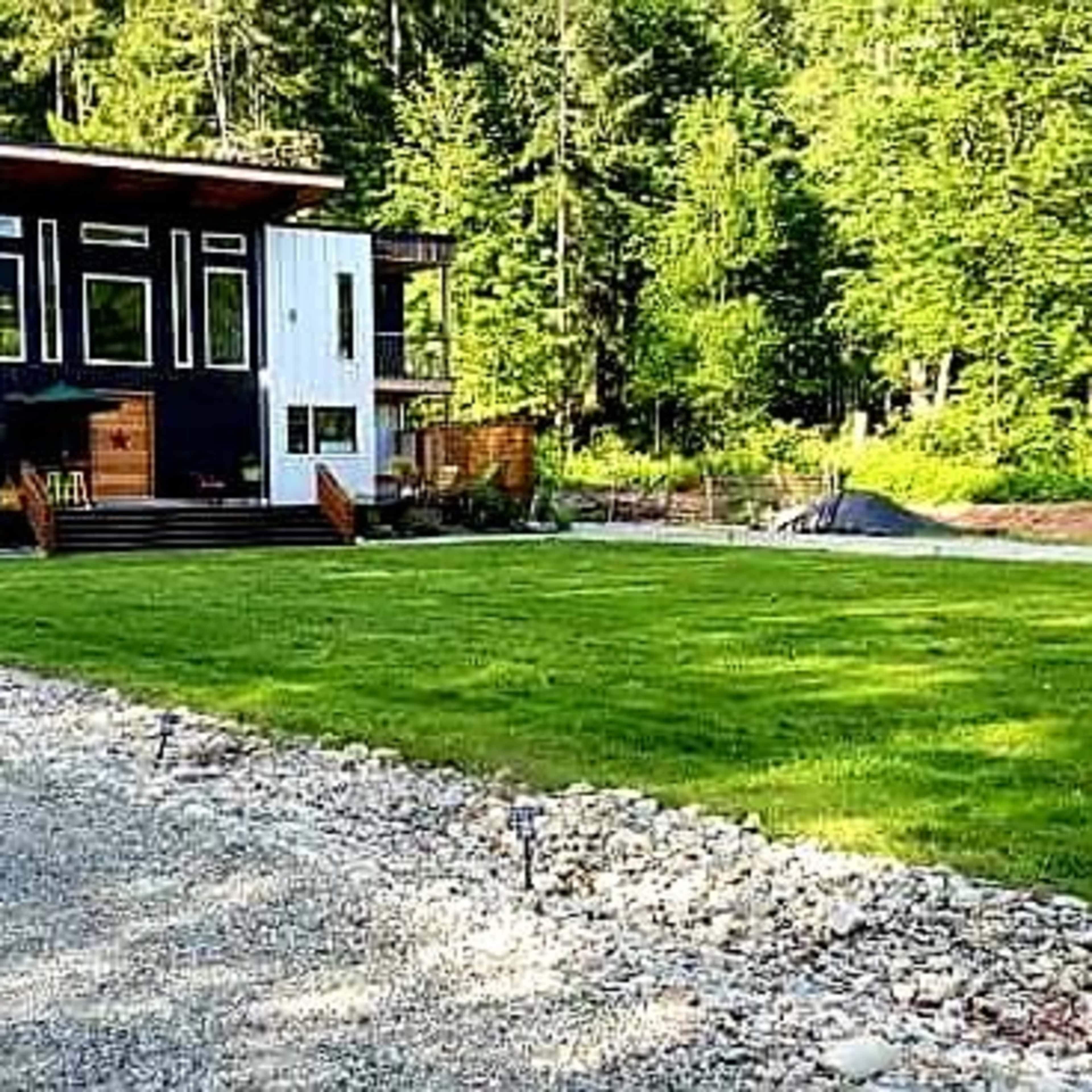 A modern two-story house with a black and white exterior is situated on a grassy lawn surrounded by trees.