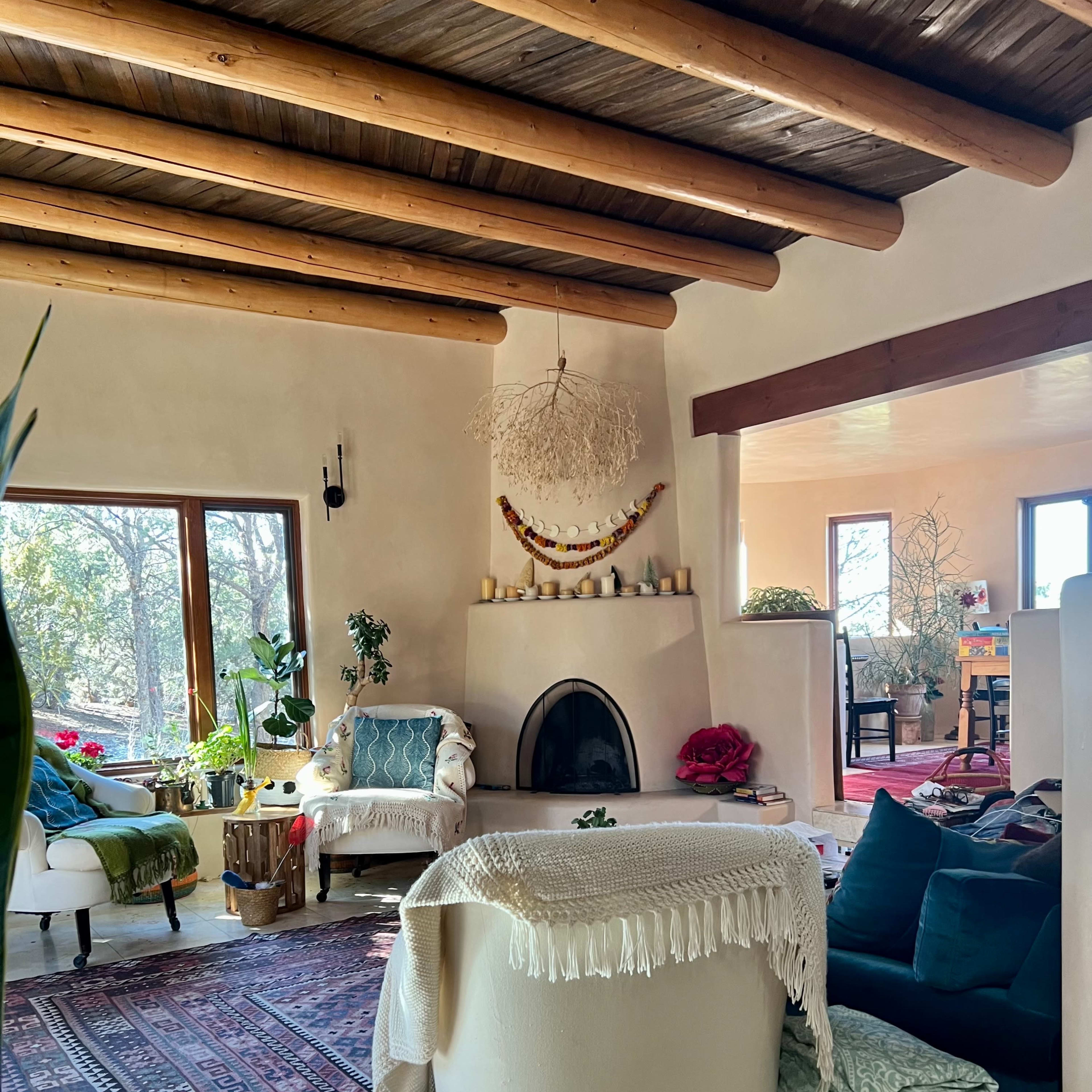 A cozy living room with a fireplace, wood-beamed ceiling, and a mix of seating arrangements, including a large white chair and various decorative elements.
