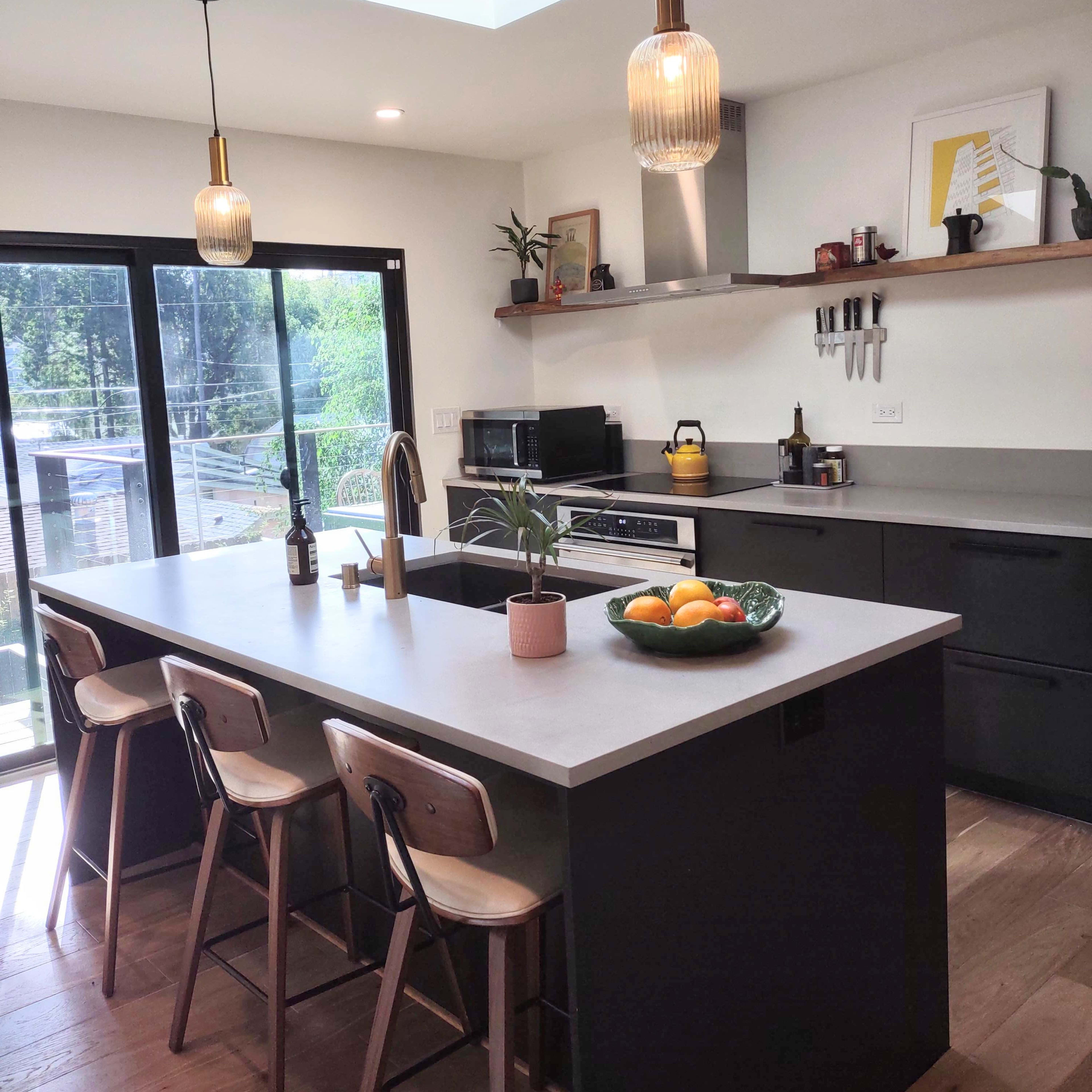 A modern kitchen features a central island with bar stools, pendant lights, a skylight, and a view of the outdoors.