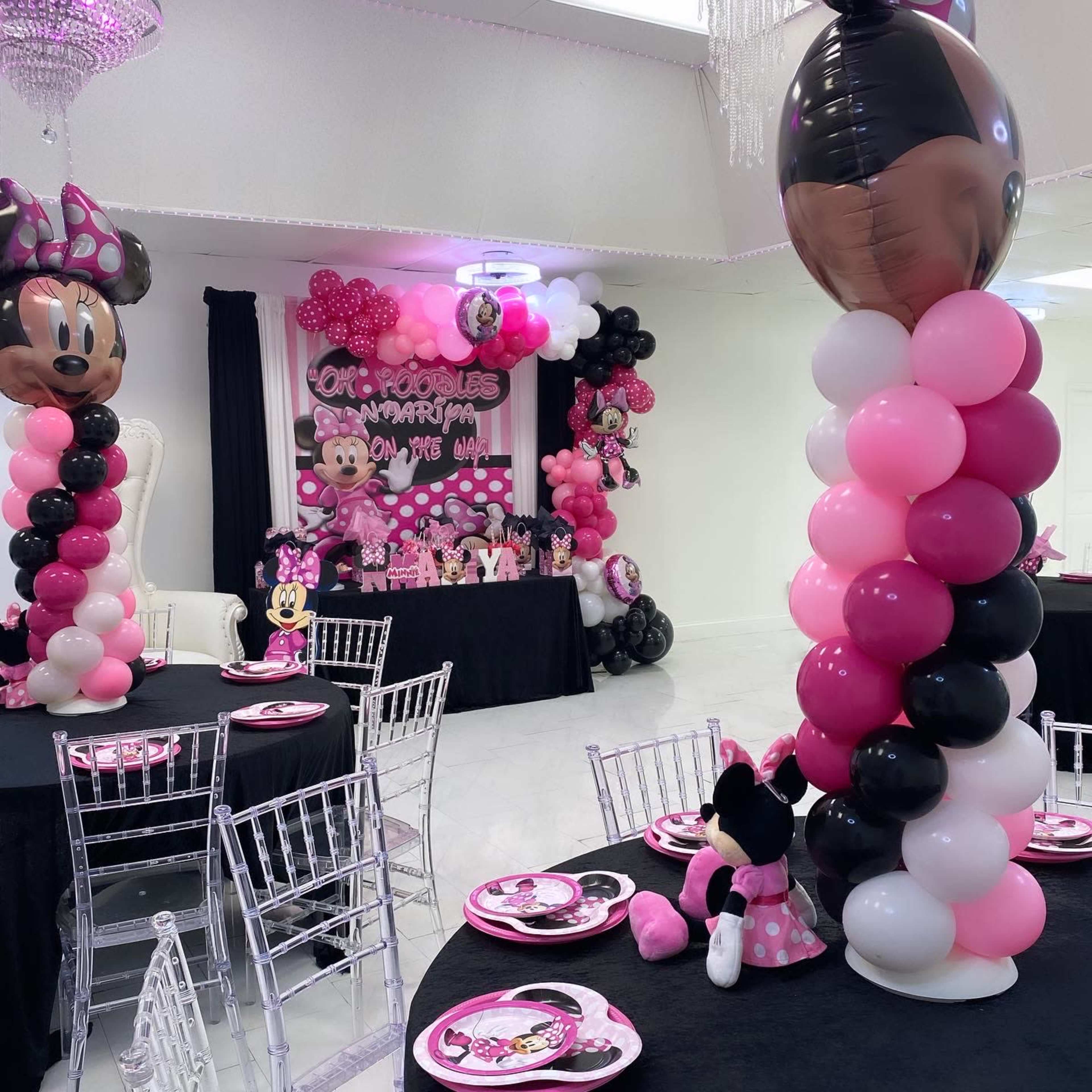 A Minnie Mouse-themed party decor with pink and black balloons, a themed backdrop, and tables set with themed plates and decorations.