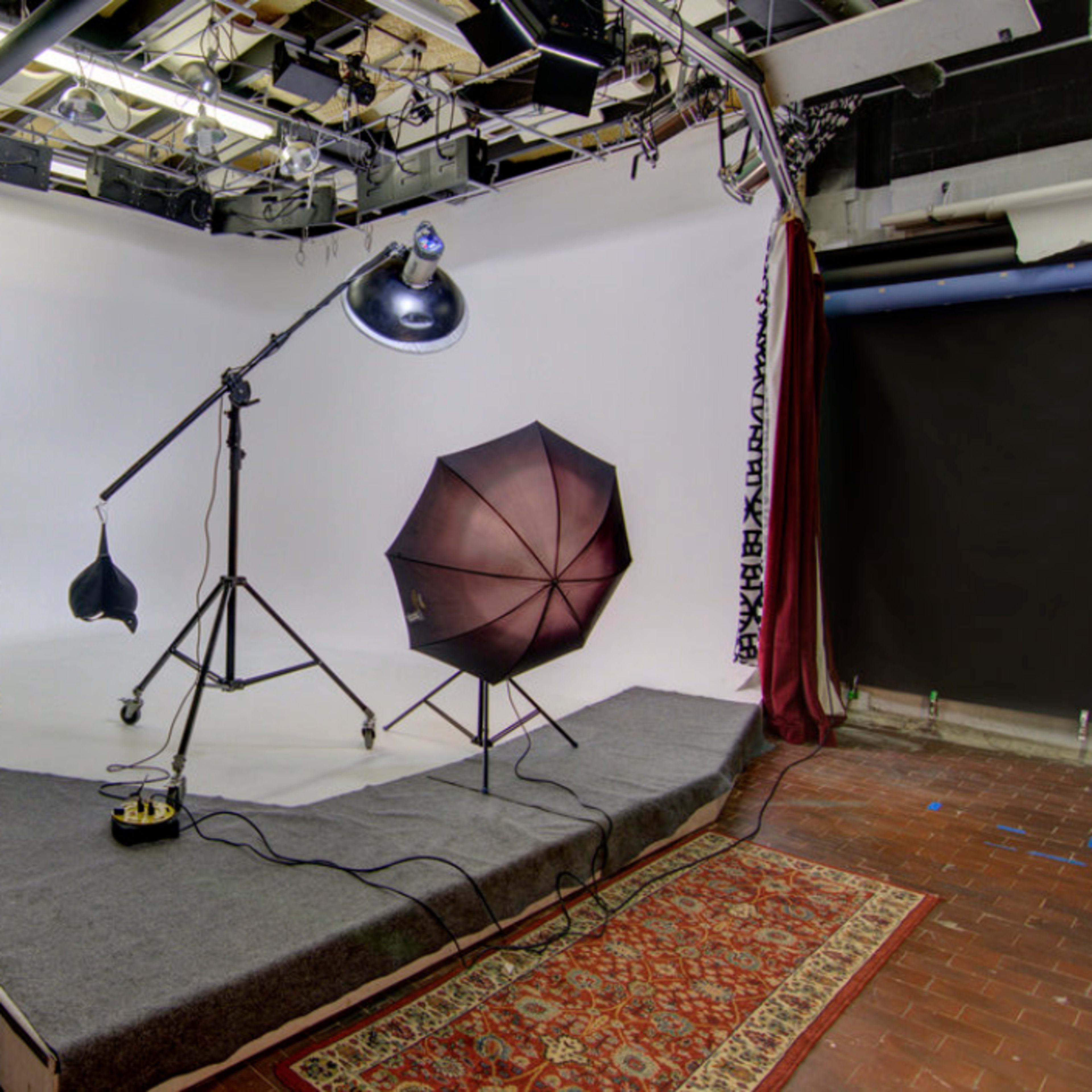 A photography studio setup with lighting equipment, a backdrop, and a patterned rug on the floor.
