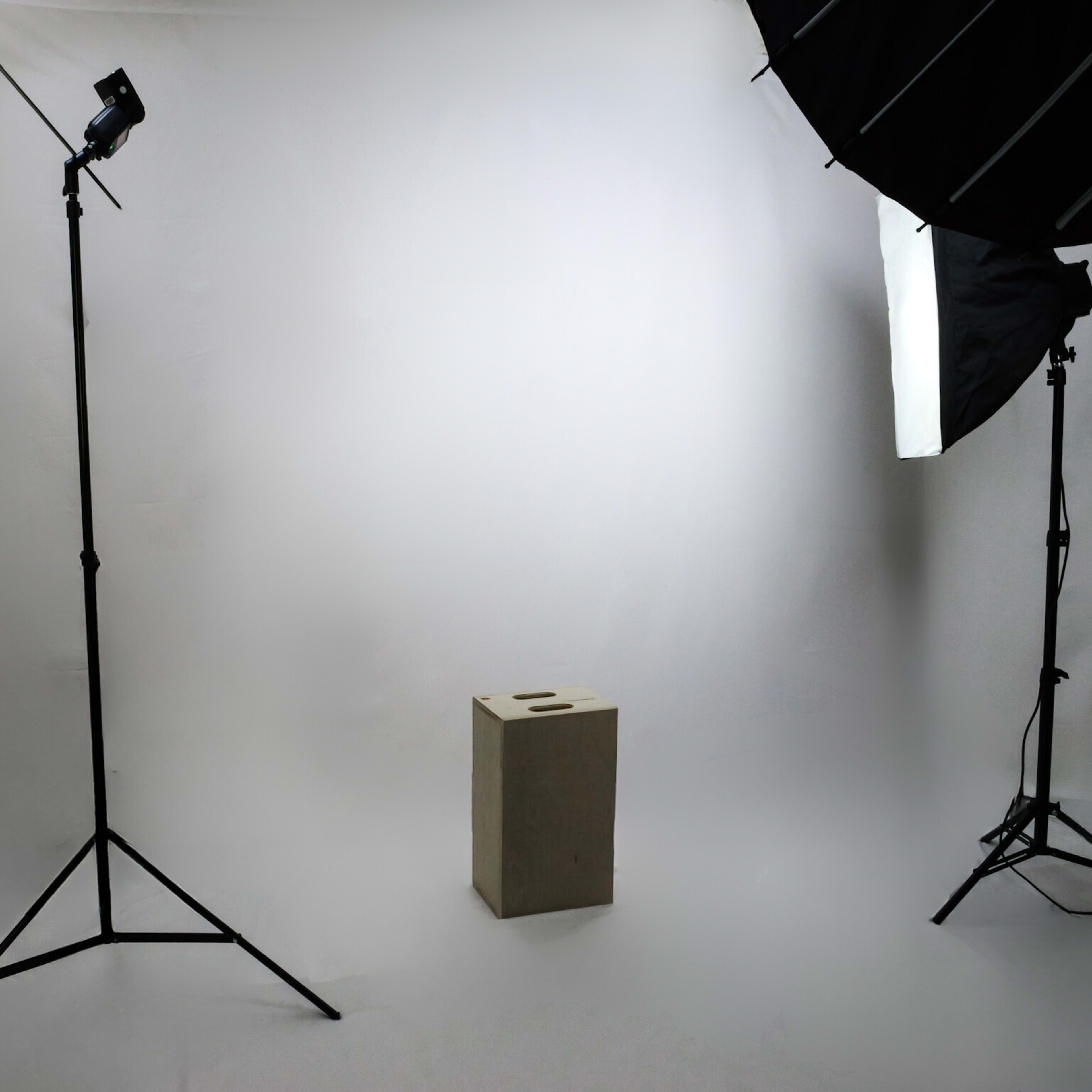 A photography studio is set up with two softbox lights and a plain backdrop, featuring a small pedestal in the center.