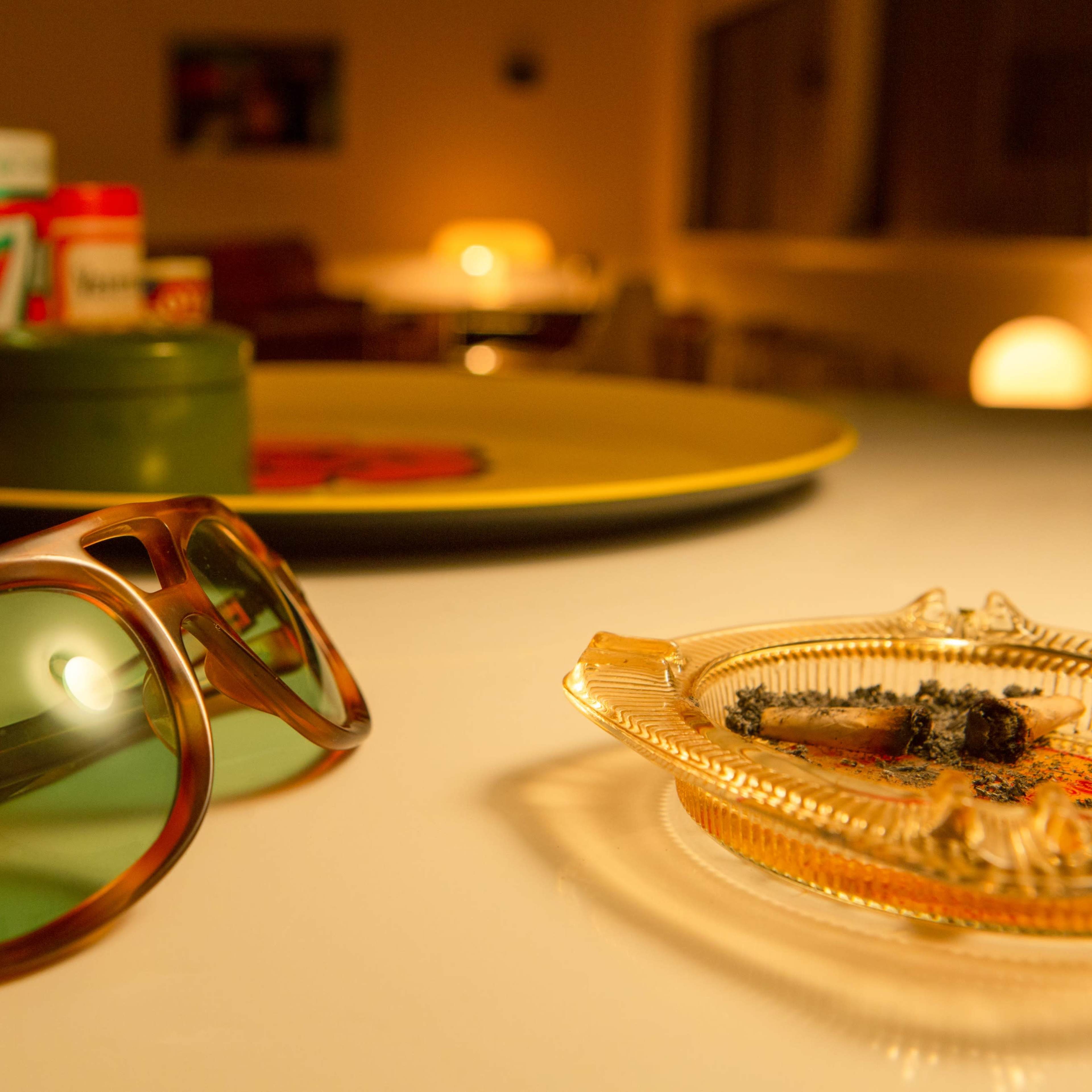 A pair of sunglasses and an ashtray with remnants are placed on a table in a softly lit room.