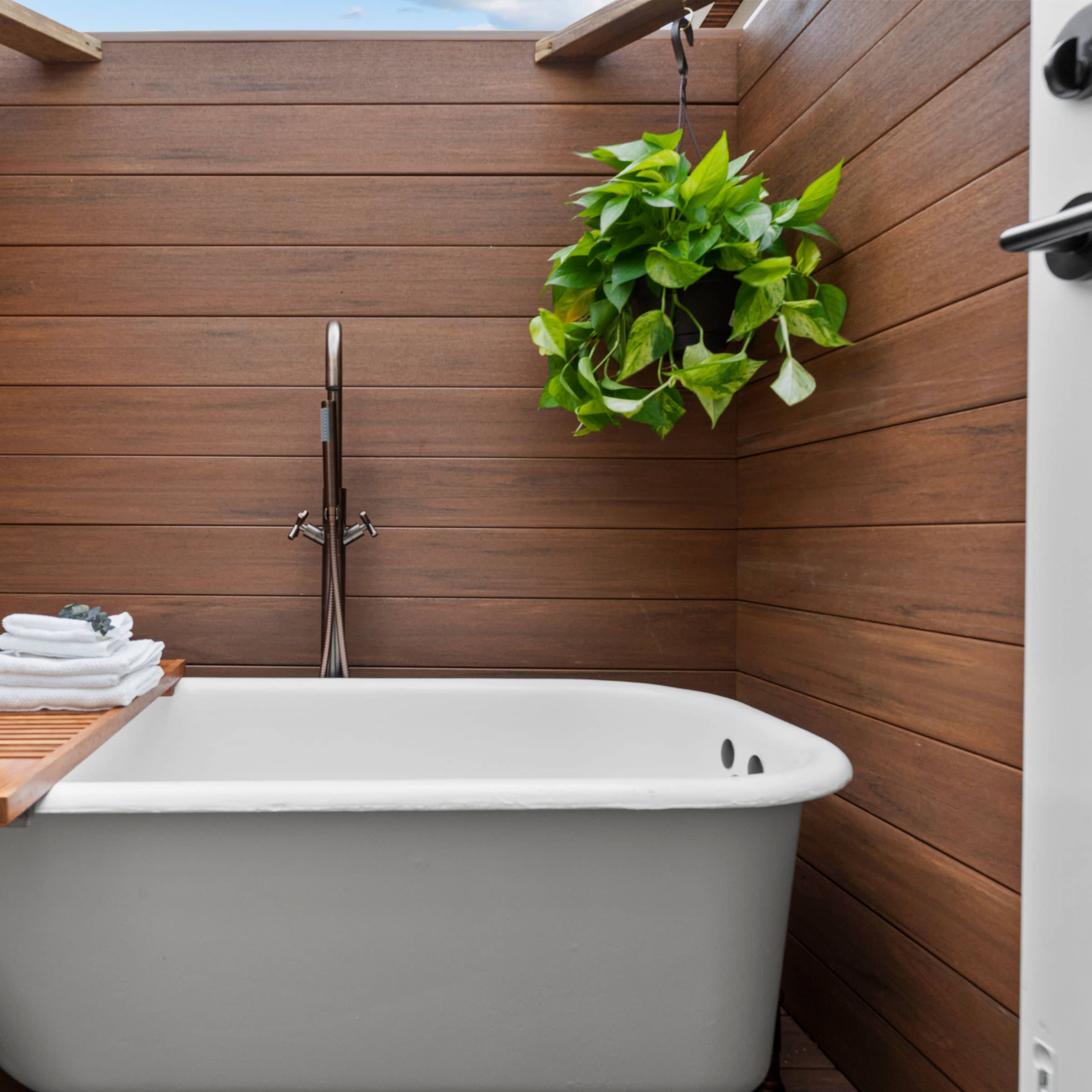 A modern, freestanding bathtub surrounded by wooden walls and a hanging plant.