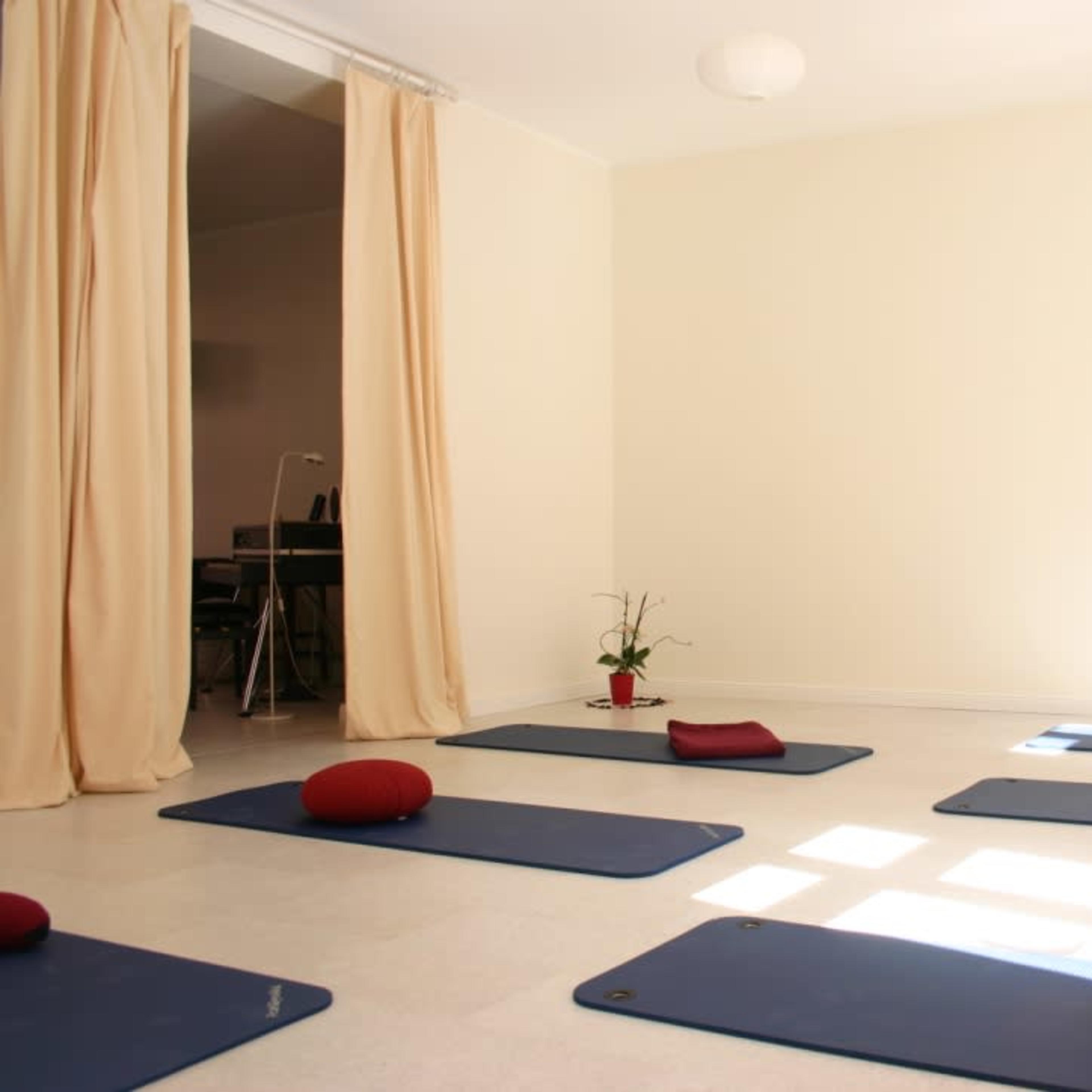 A clean, minimalistic yoga studio with blue mats arranged on the floor and red cushions placed on some of them.