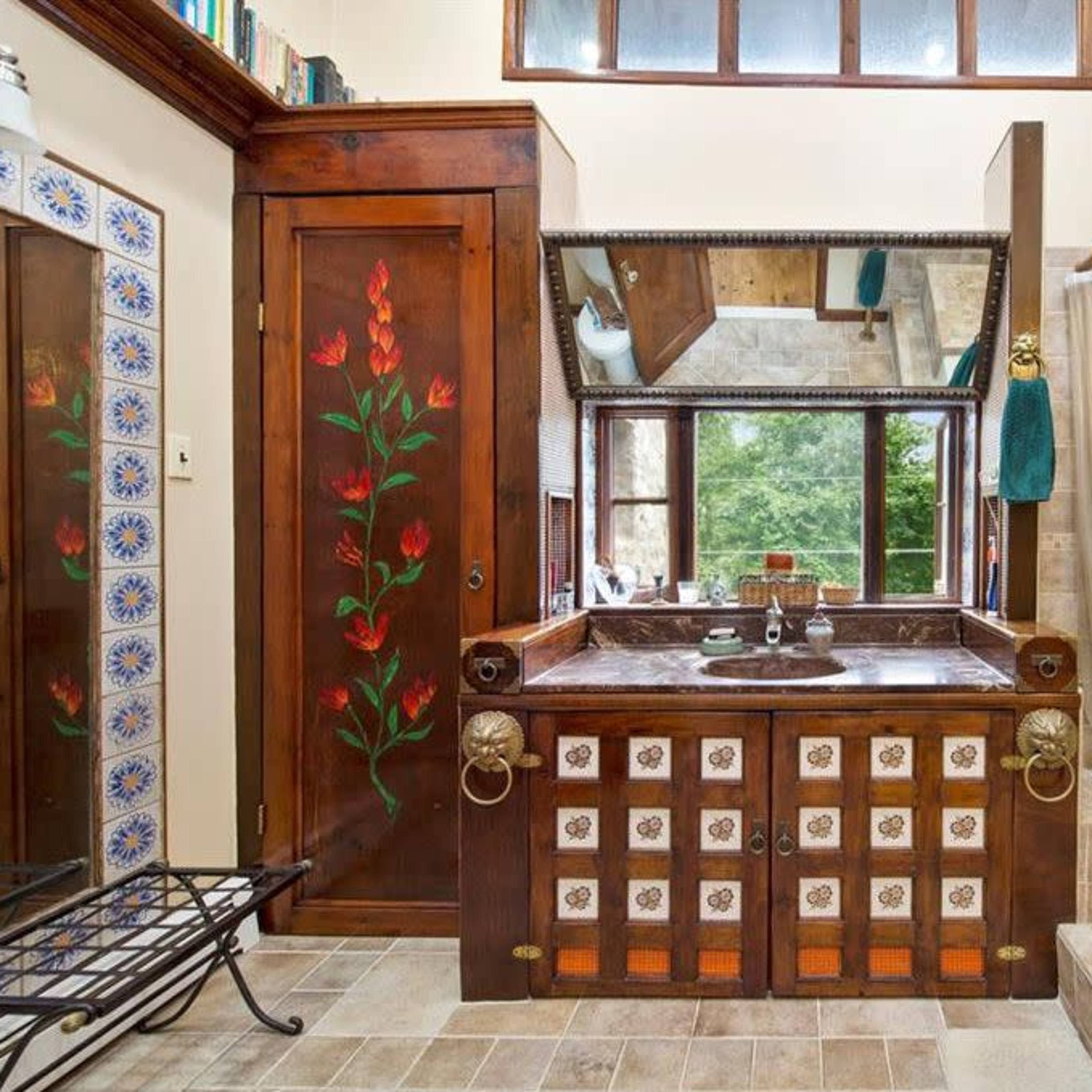 A bathroom featuring a wooden vanity with floral designs, a bathtub, and large windows allowing natural light.