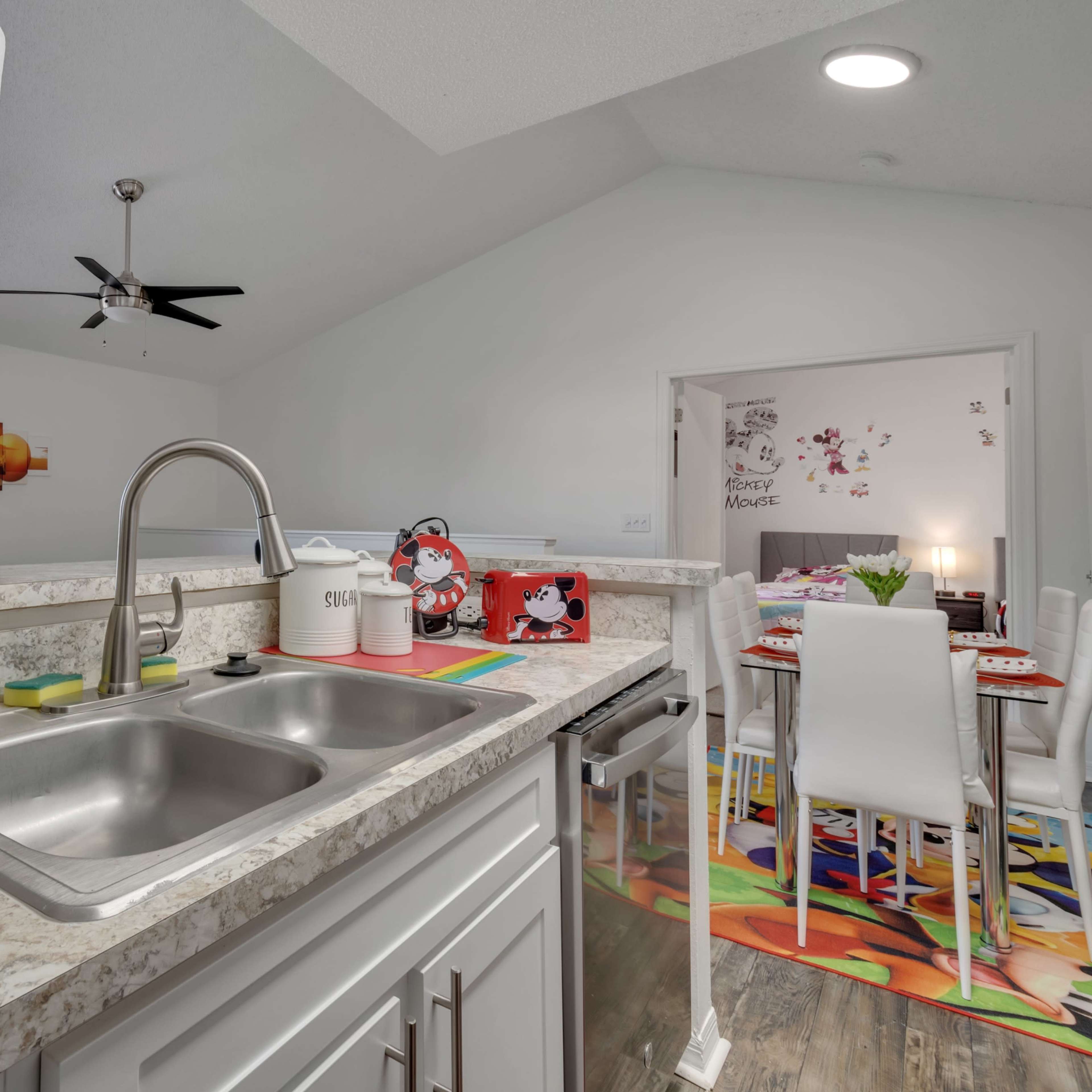 A modern kitchen features a double sink, a blender on the counter, and a view towards a dining area with colorful decor.