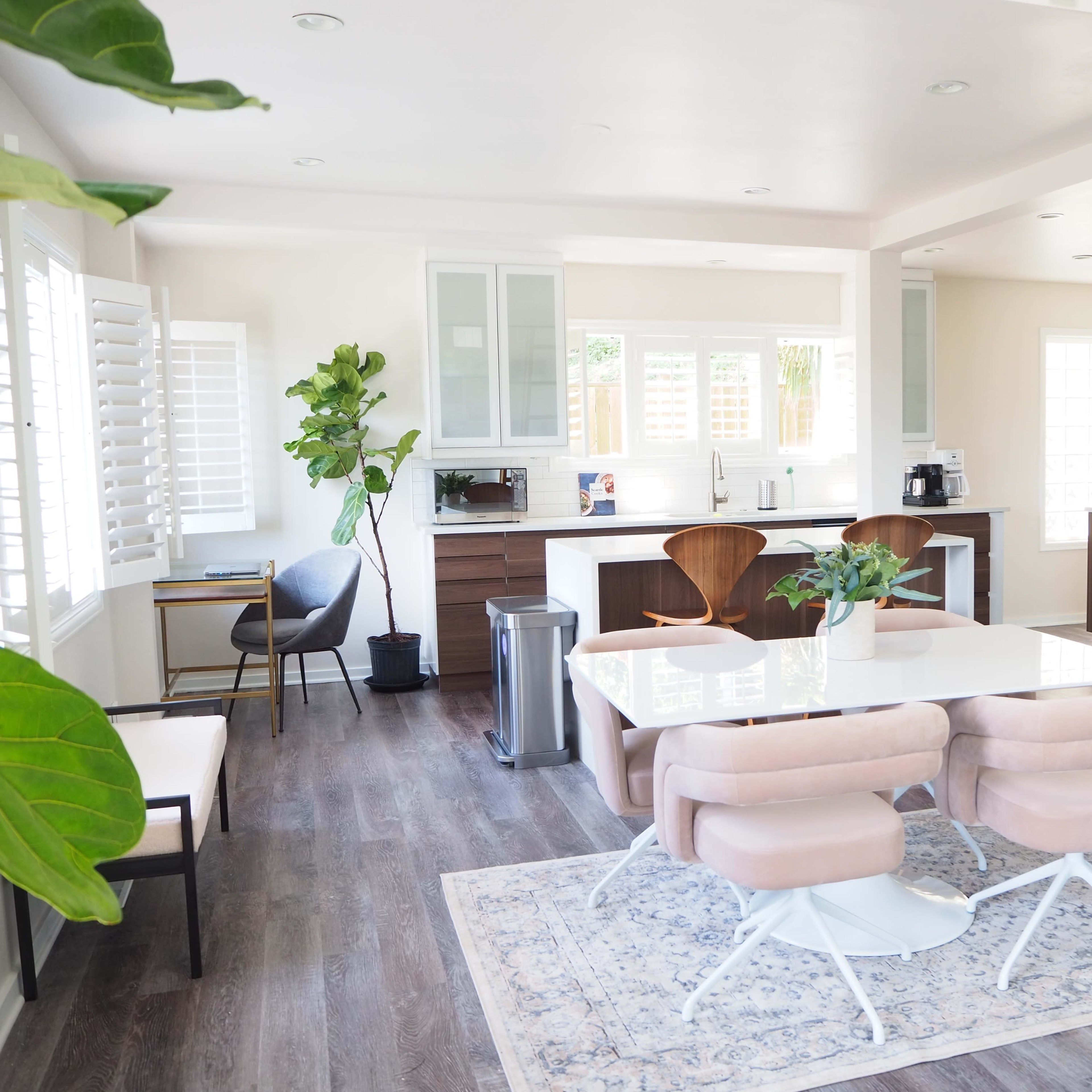 A modern kitchen and dining area with a white table, pink chairs, and a wooden ladder leading to a loft space.