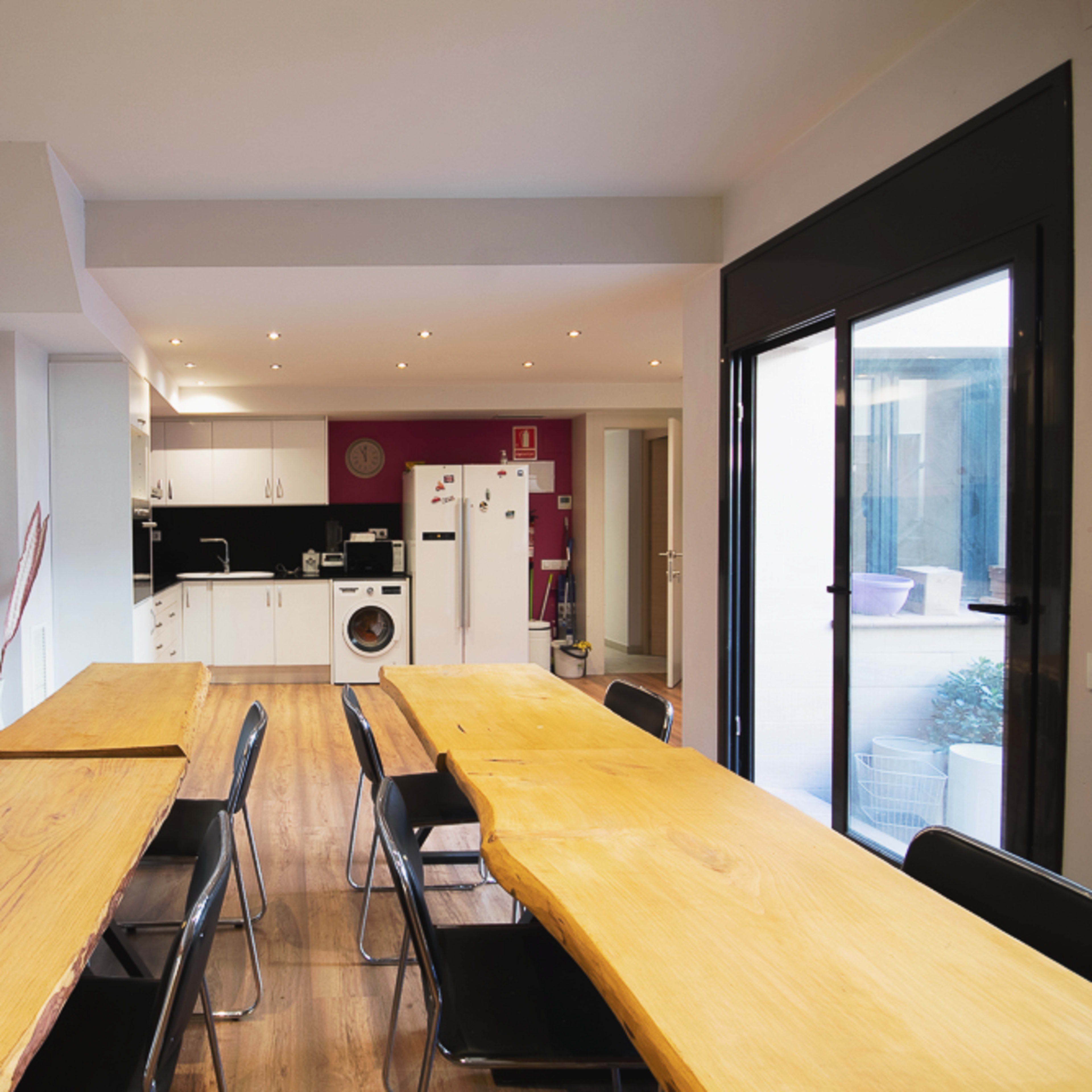 A spacious dining area features long wooden tables and black chairs, leading to a modern kitchen with white cabinetry and appliances.