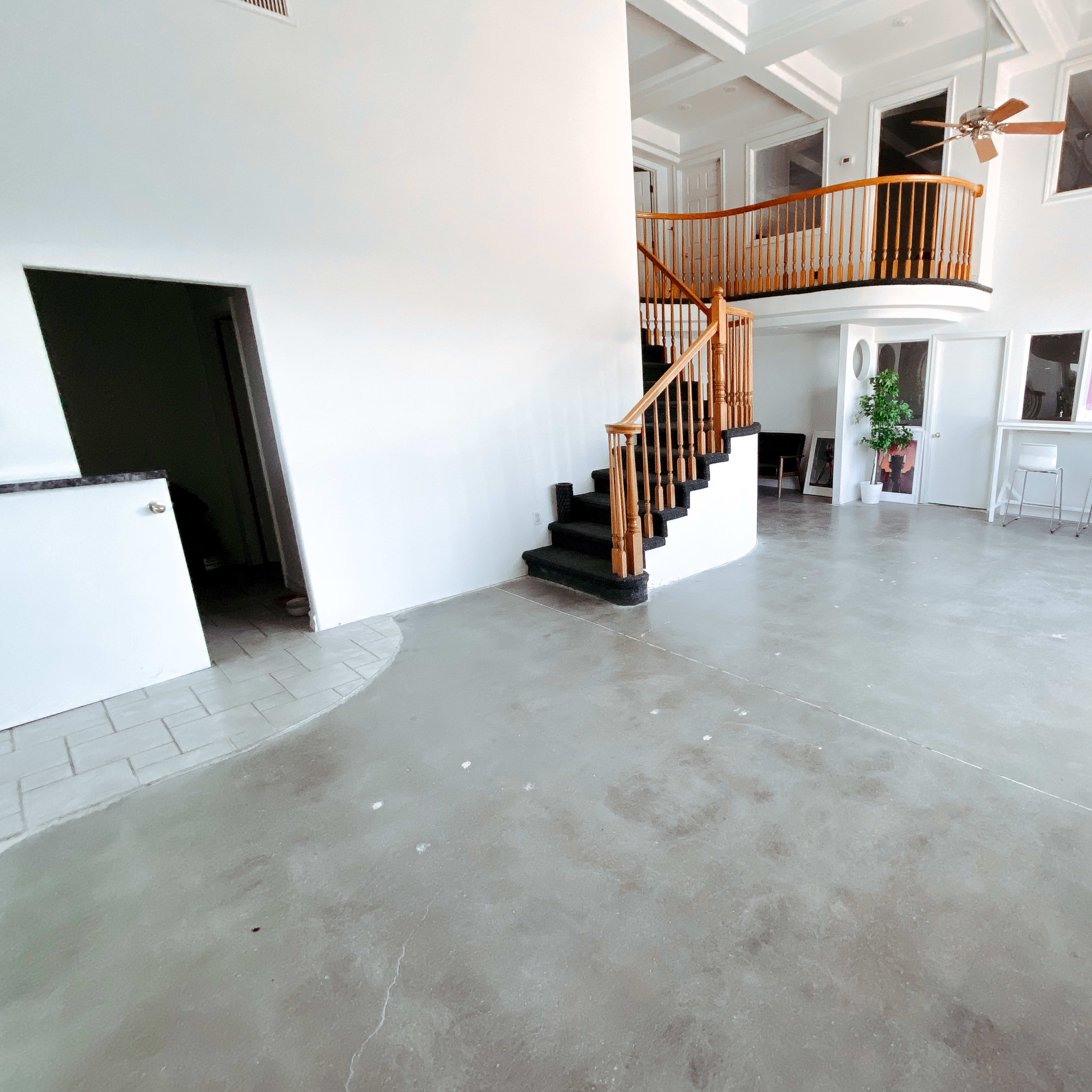 A spacious, open-concept living area featuring a staircase with wooden railing, large windows, and a minimalist design with a concrete floor.