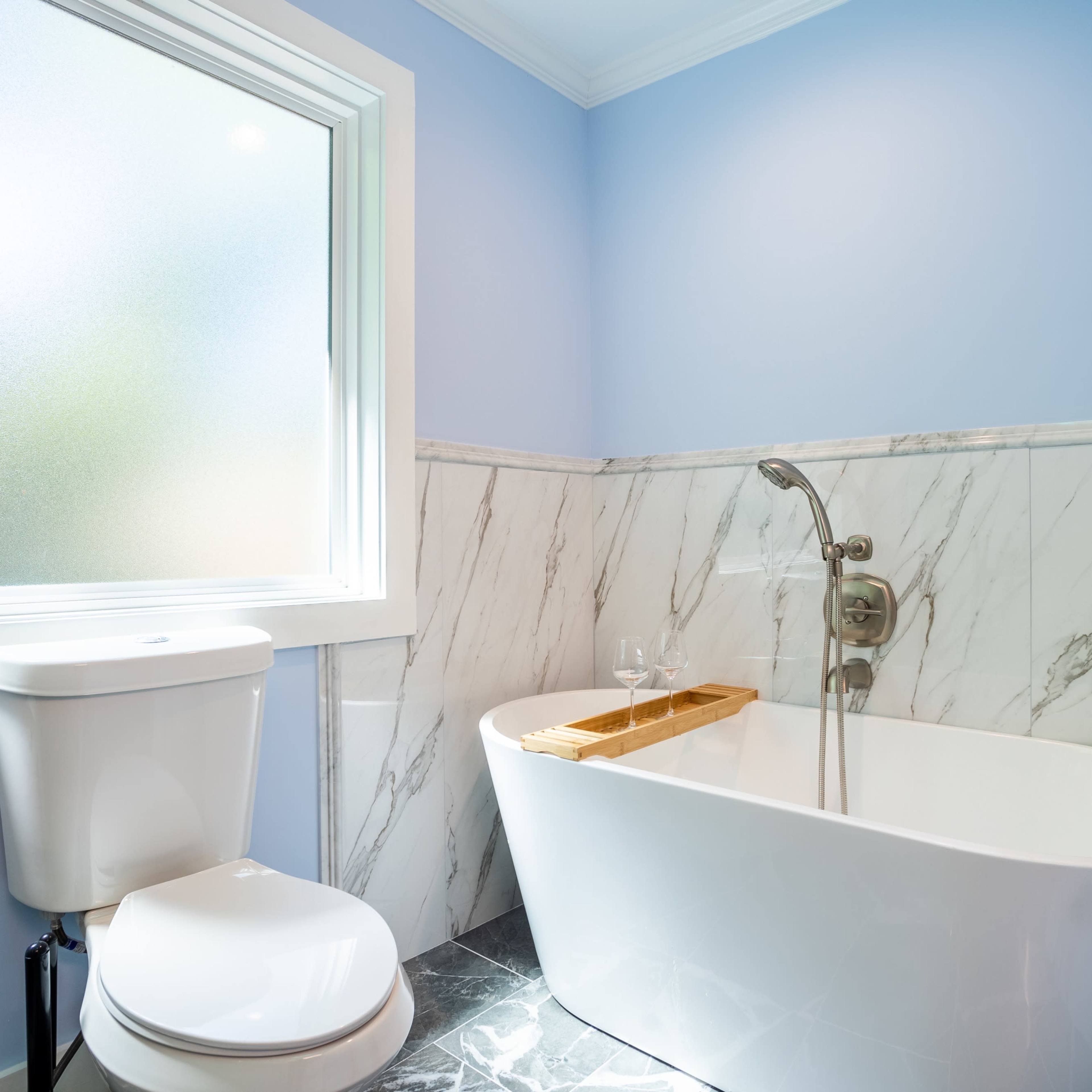 A bathroom featuring a freestanding bathtub, a toilet, a frosted window, and marble-like wall accents.
