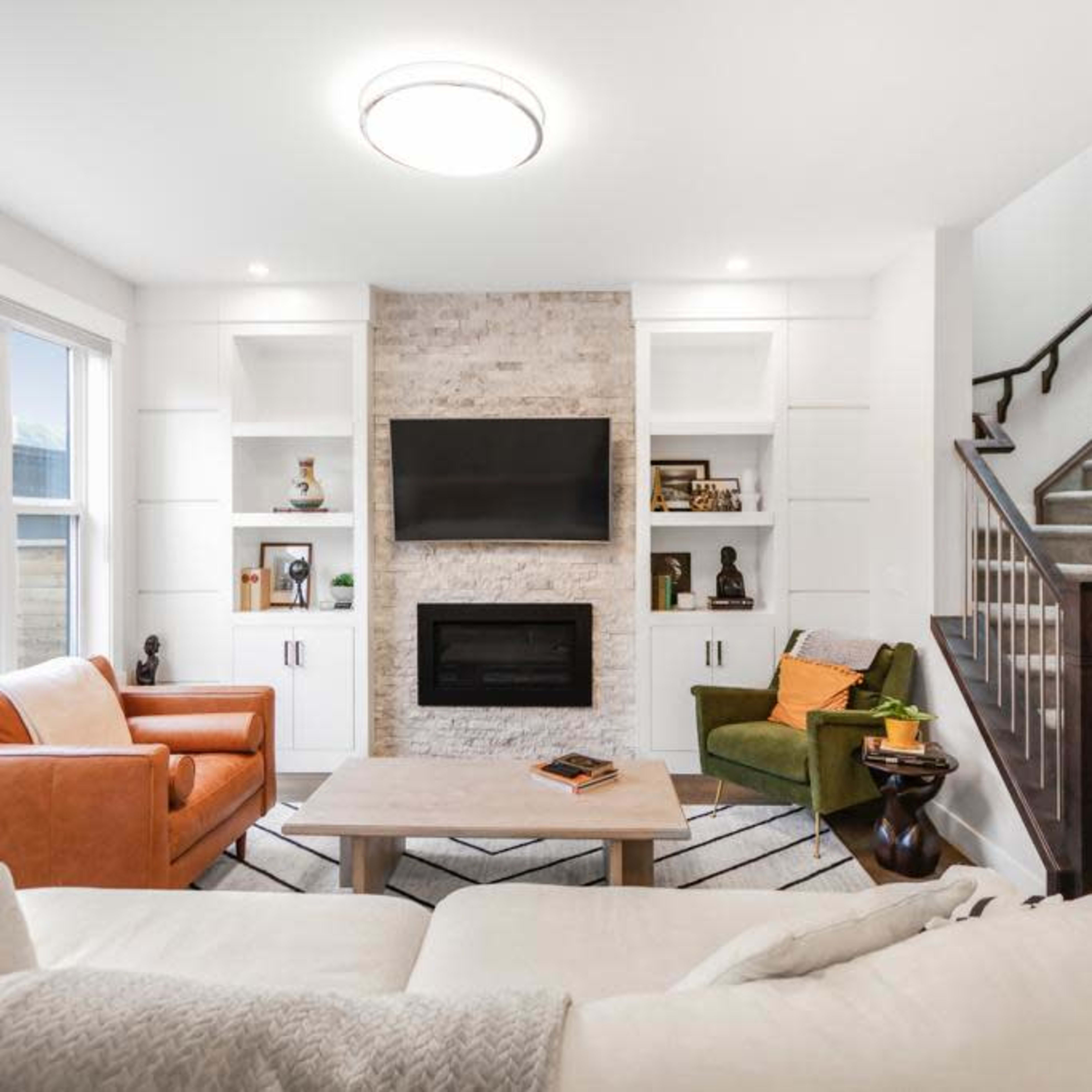 A modern living room featuring a fireplace with a TV above it, flanked by built-in shelves, and a staircase in the background.