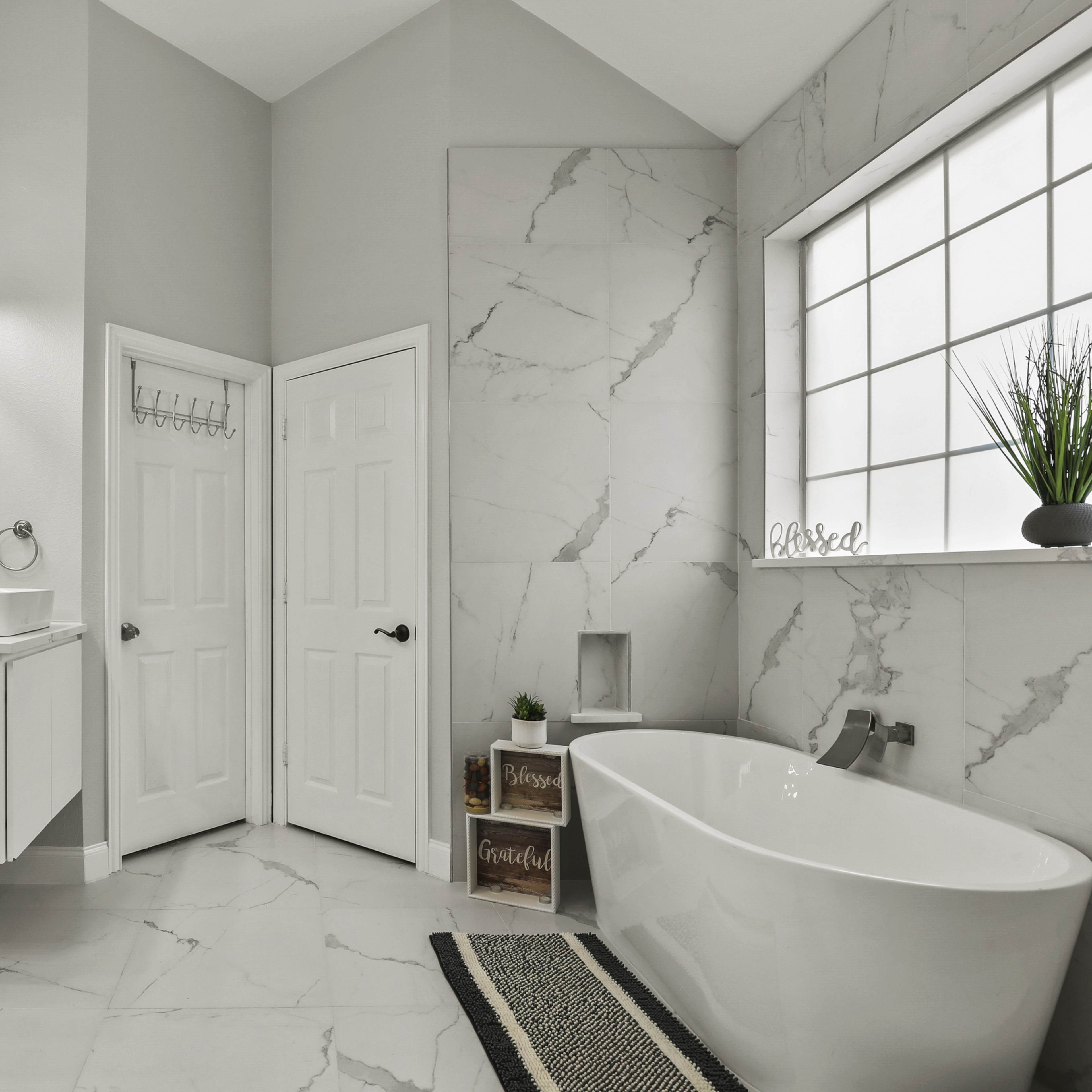 A modern bathroom featuring a freestanding tub, a double vanity with a large mirror, and marble-patterned walls and flooring.
