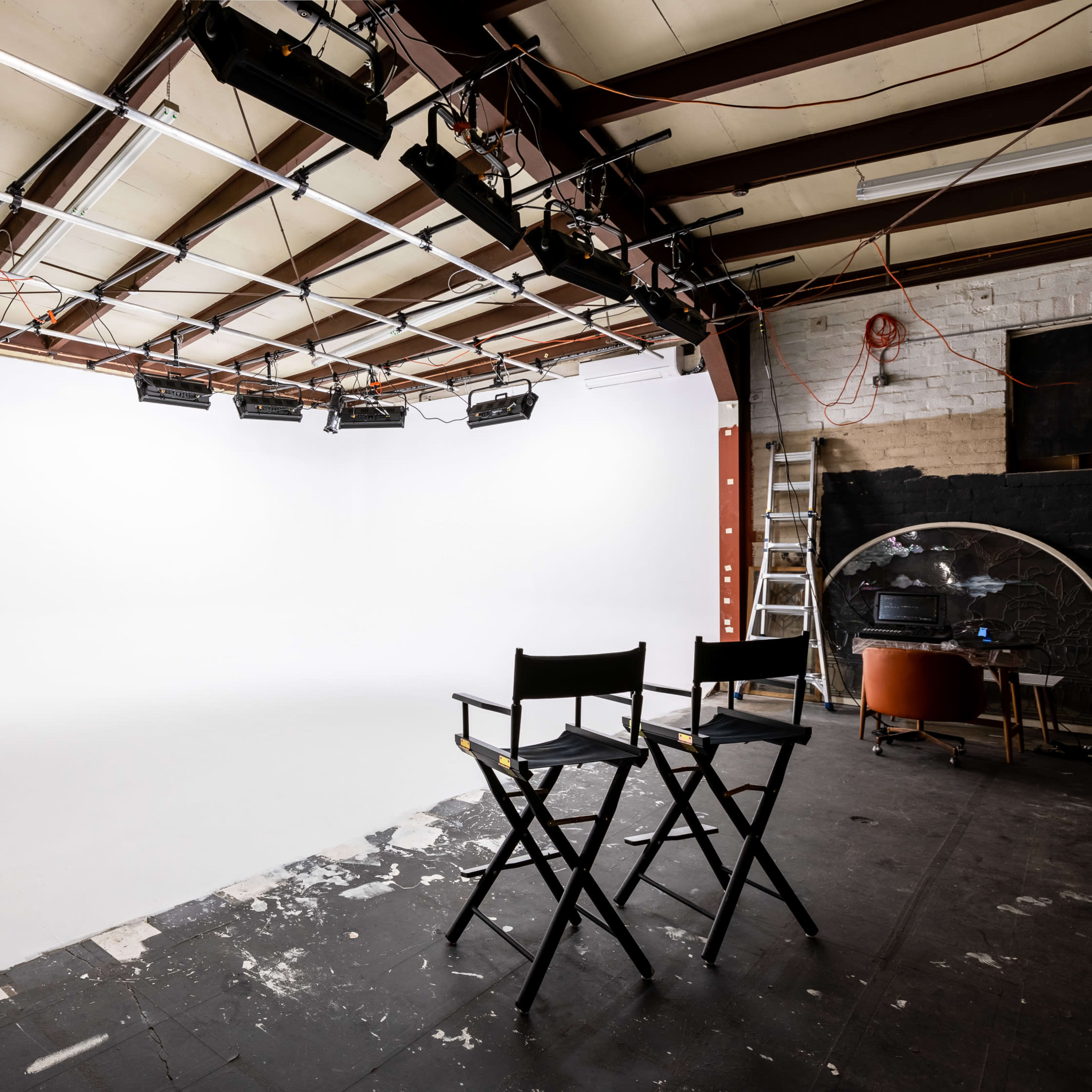 A spacious photography studio features a white backdrop, two director's chairs, and overhead lighting fixtures.