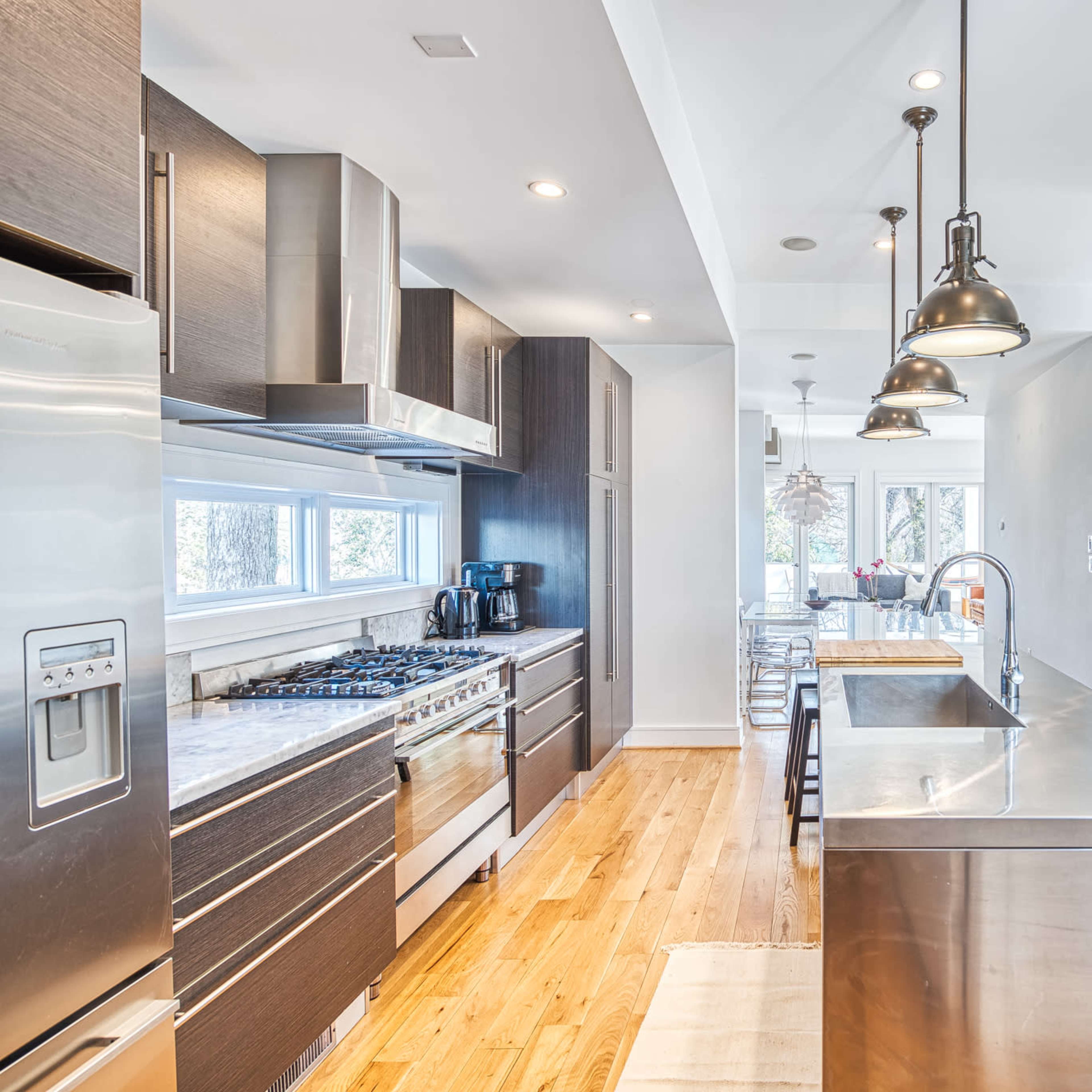 A modern kitchen features stainless steel appliances, dark cabinetry, a central island, and pendant lighting.