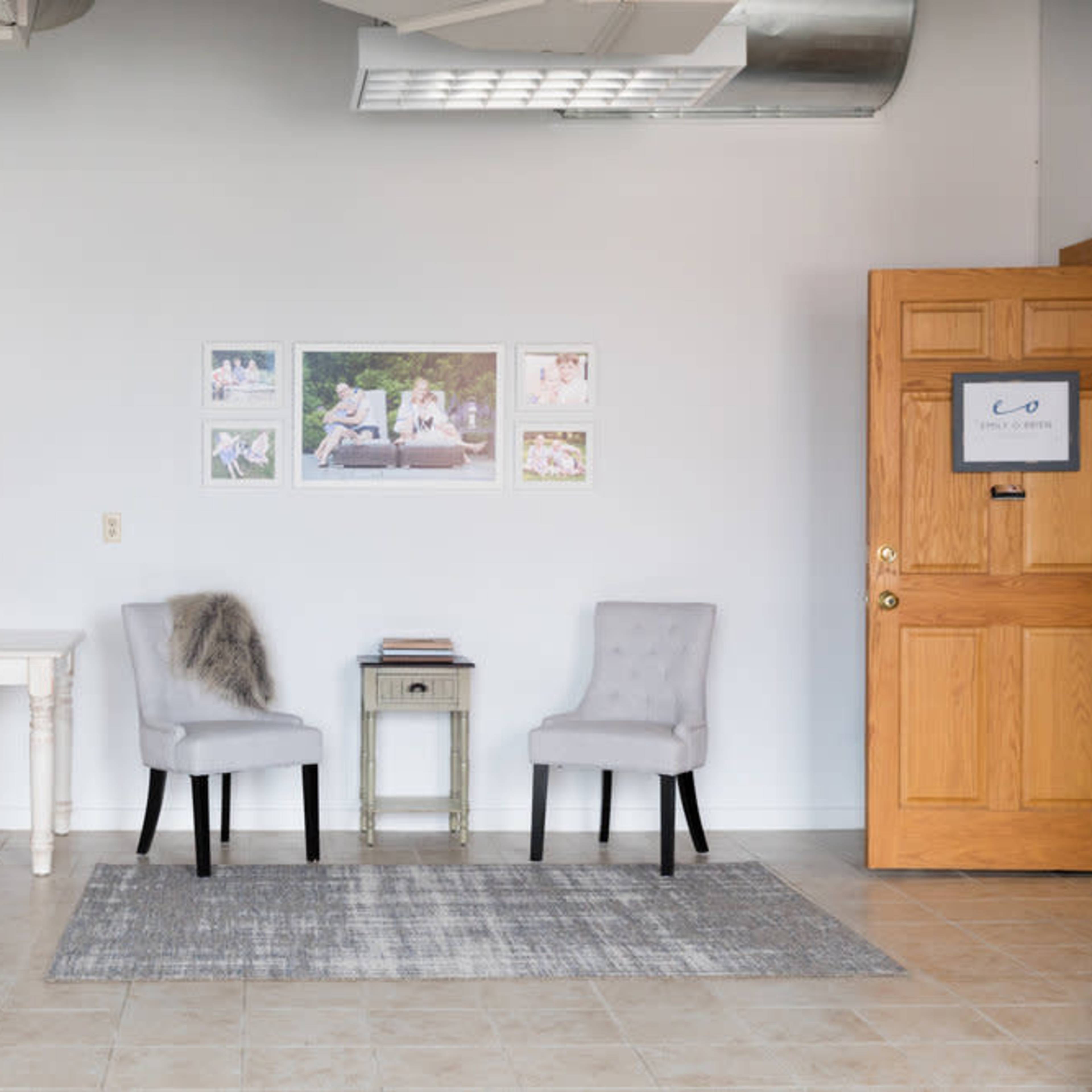 A modern office space with a desk, computer, and various chairs arranged alongside a door and framed photos on the wall.